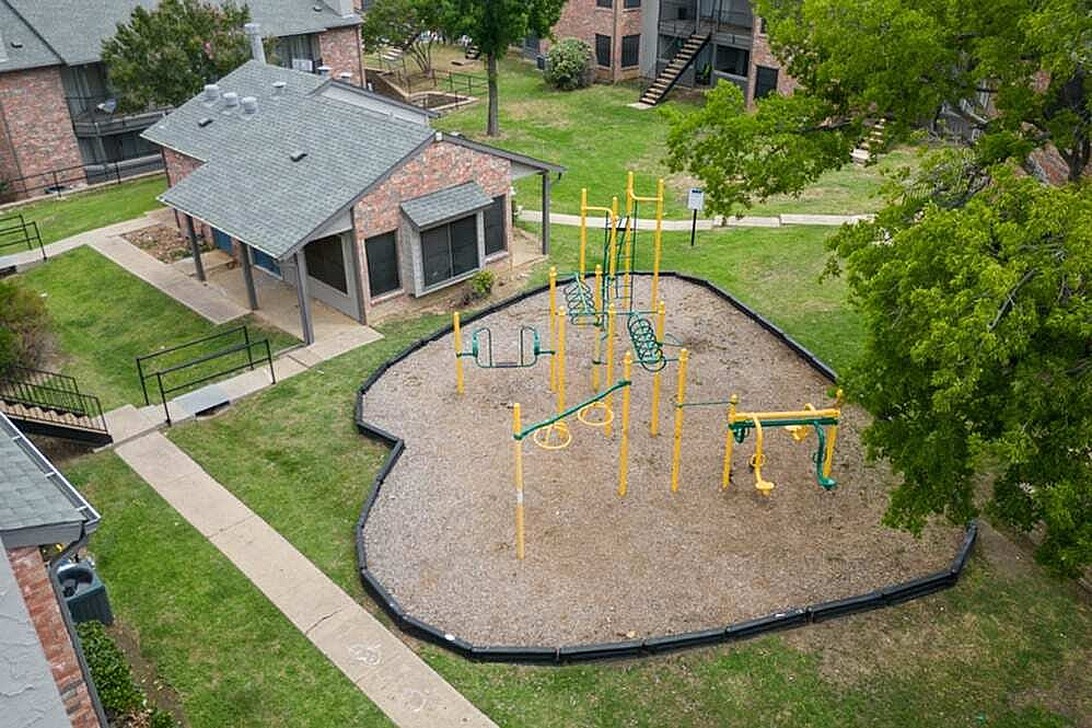 Charming aerial view of a well-maintained playground surrounded by lush greenery in a cozy apartment community.
