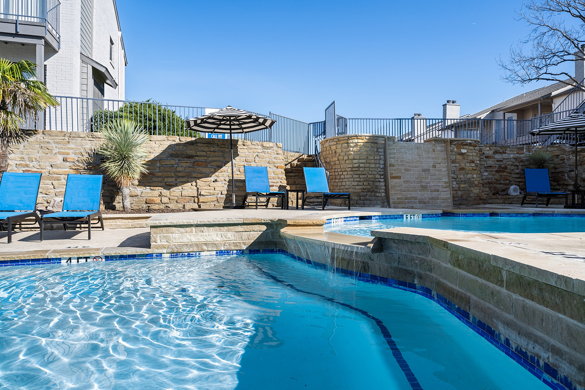Luxurious outdoor pool area featuring inviting sun loungers, vibrant blue water, and elegant stone landscaping under a clear blue sky.