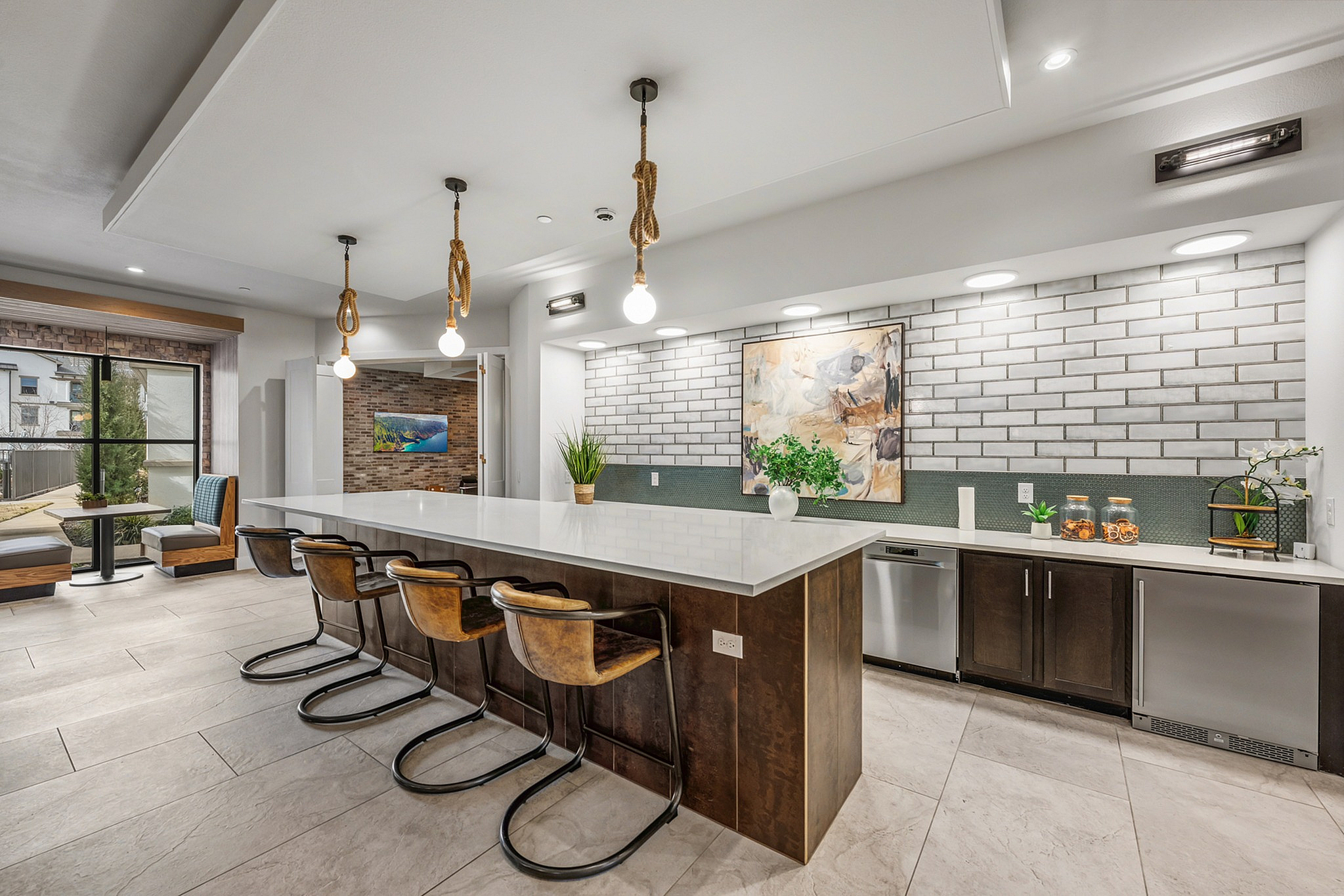 Sleek modern kitchen with a spacious island, industrial pendant lights, and cozy dining nook overlooking a garden view.