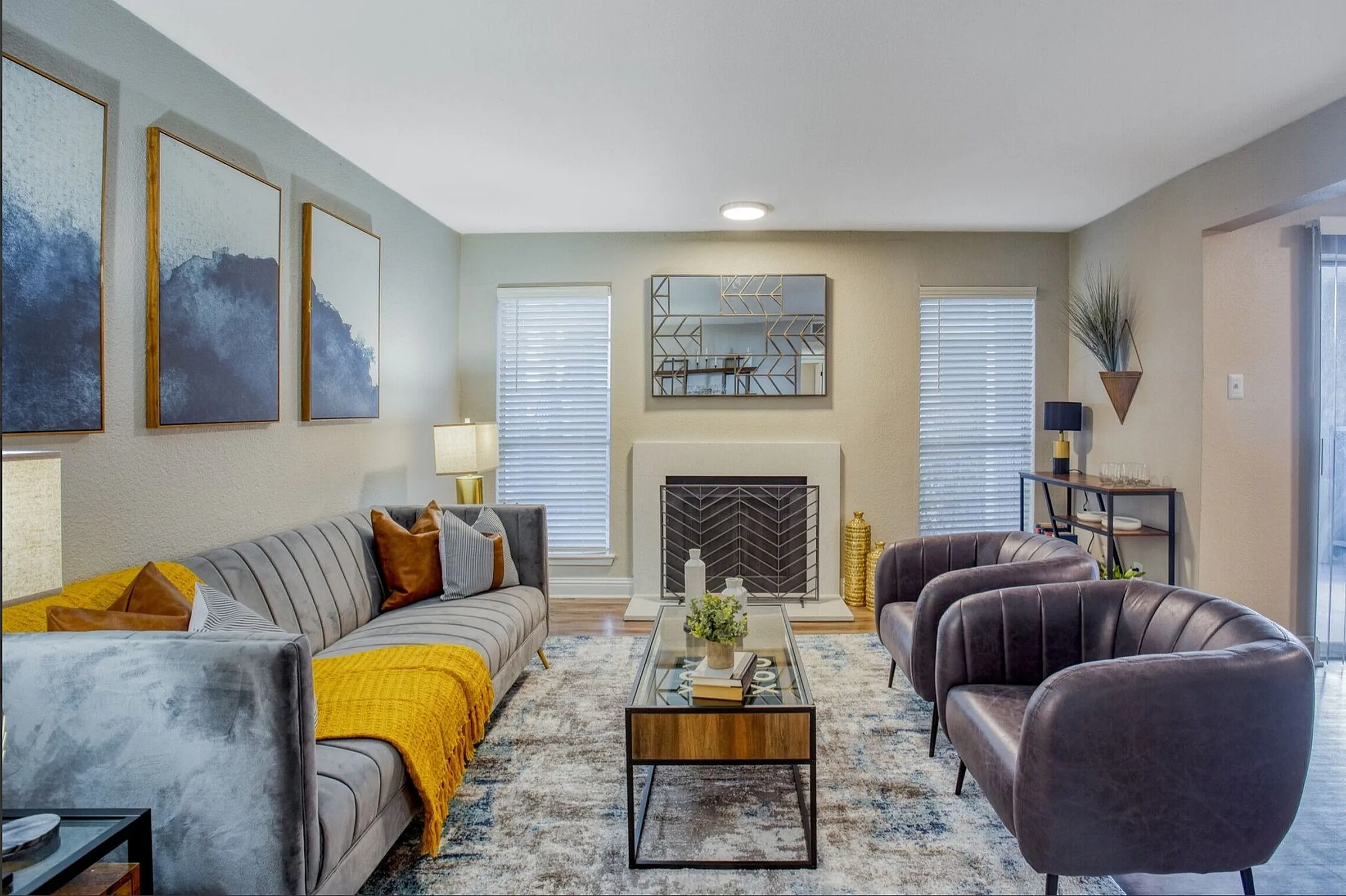 Elegant living room with modern decor, featuring a plush gray sofa, stylish armchairs, geometric artwork, and a sleek fireplace design.