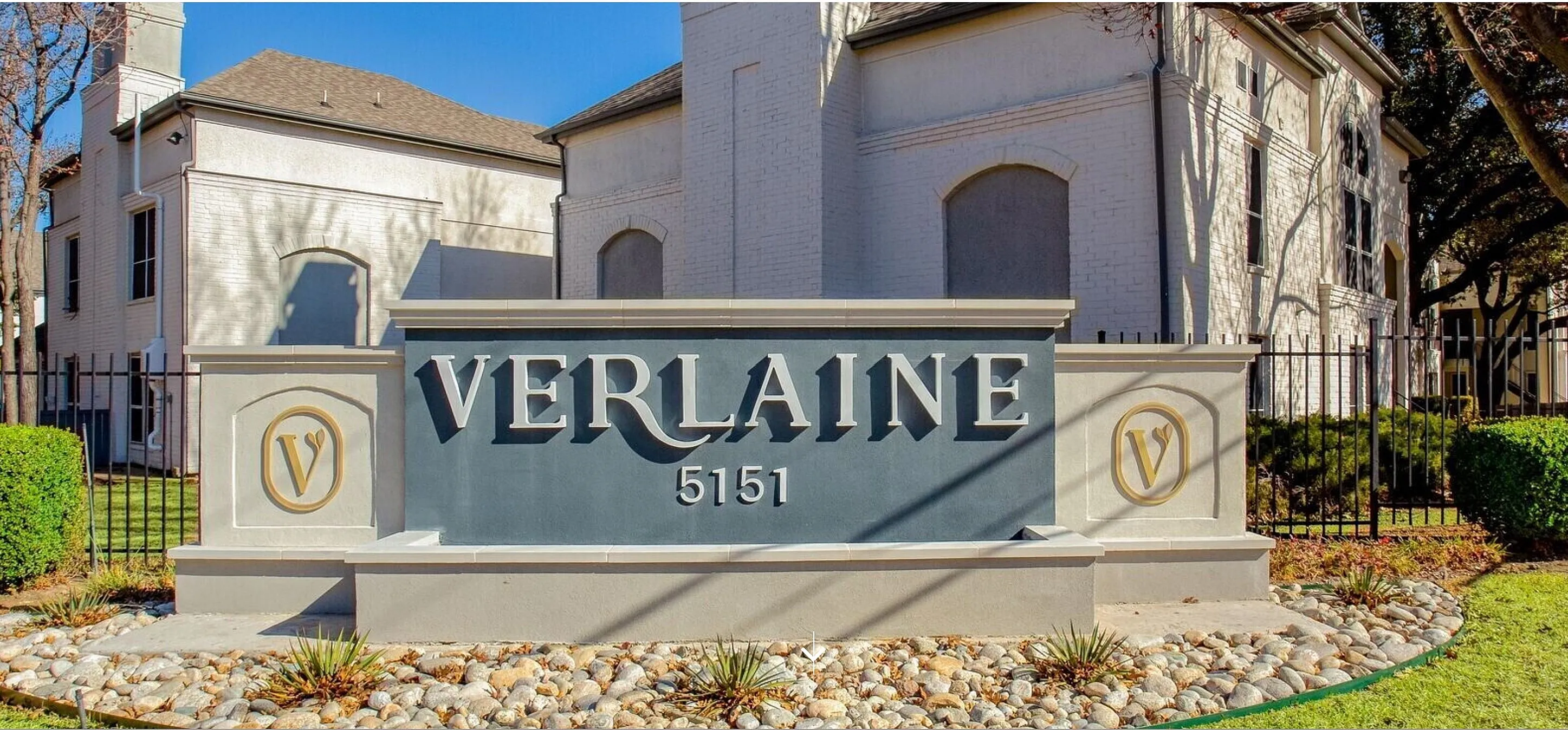Elegant exterior of Verlaine Apartments with a stylish entrance sign amidst lush greenery and classic architecture.