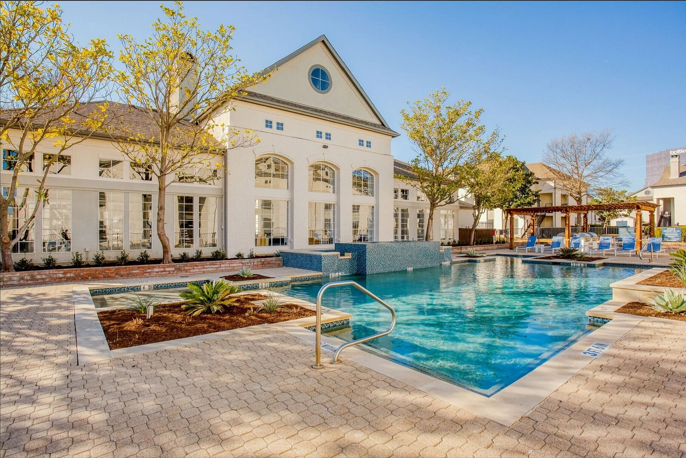 Luxurious outdoor pool area with elegant white brick architecture, surrounded by lush landscaping and relaxing sun loungers.