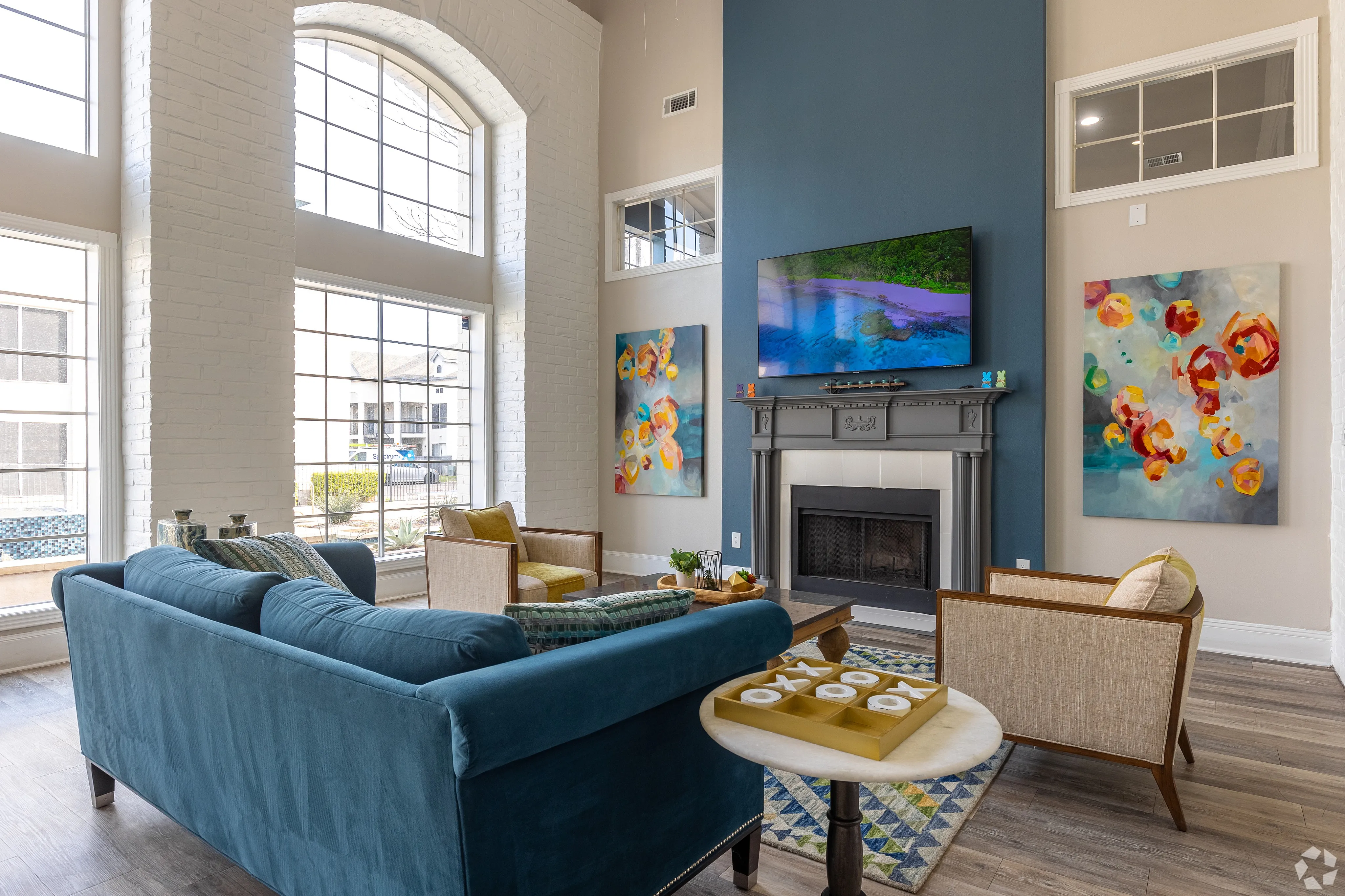Elegant living room with high ceilings, large windows, vibrant artwork, and a cozy fireplace, providing a luxurious and inviting atmosphere.