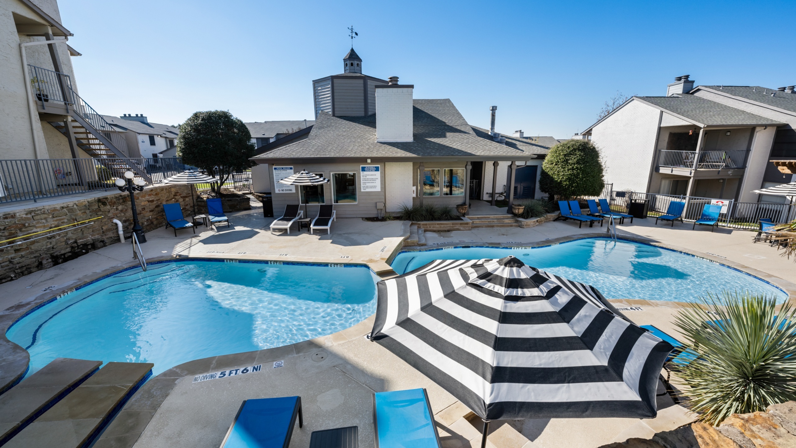 Inviting poolside retreat with chic striped umbrellas, lounge chairs, and modern apartment backdrop under a clear blue sky.