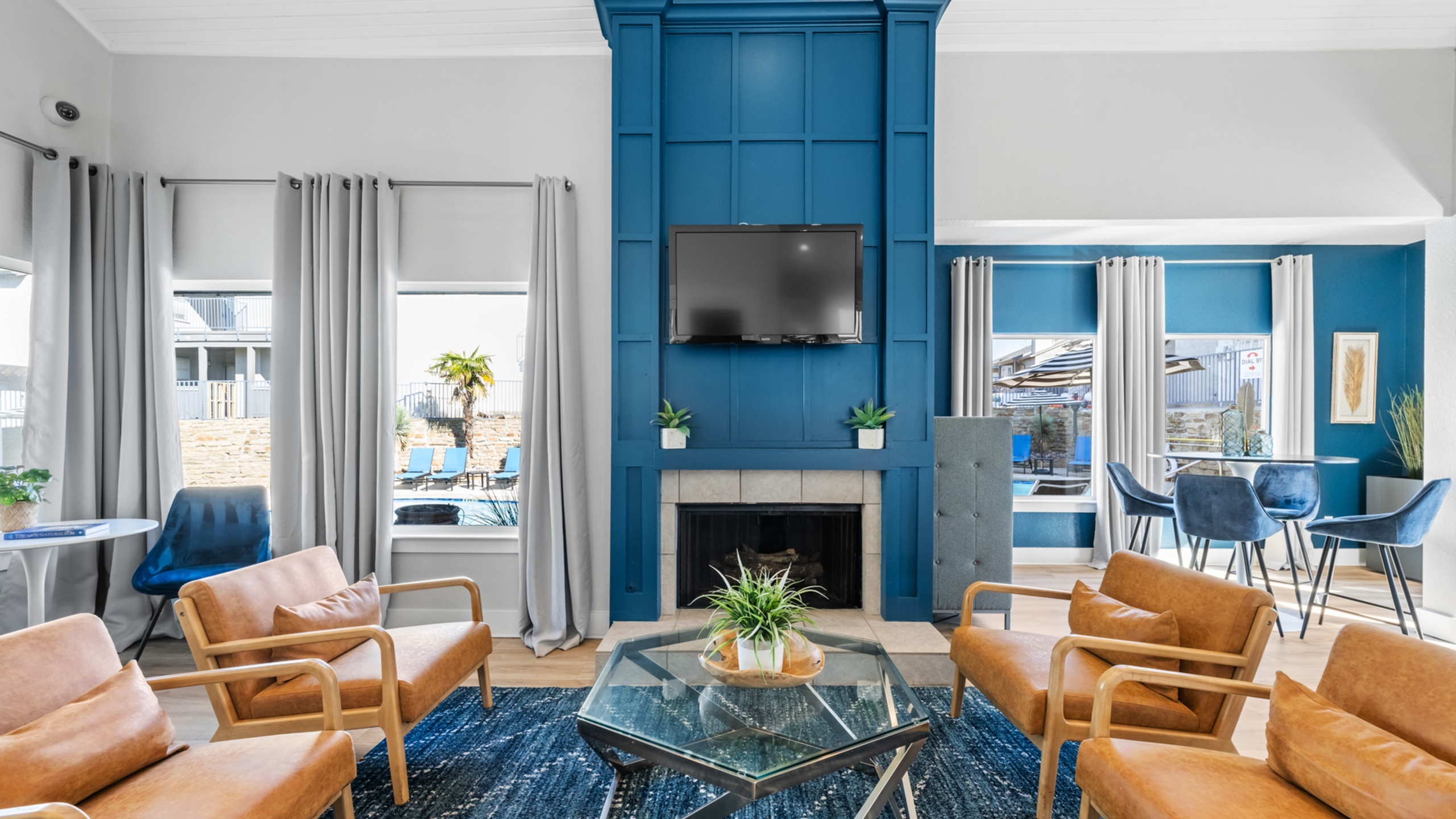 Modern living room with stylish blue accent wall, cozy seating area, and natural light from large windows overlooking a pool.