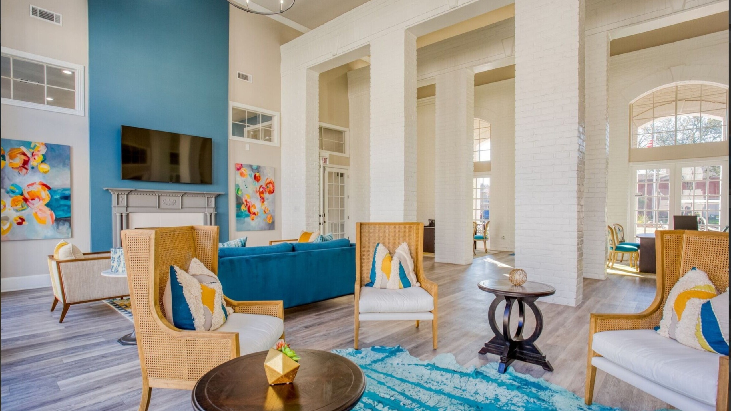 Bright and elegant living room with high ceilings, featuring vibrant artwork, comfortable seating, and a stylish blue accent wall.