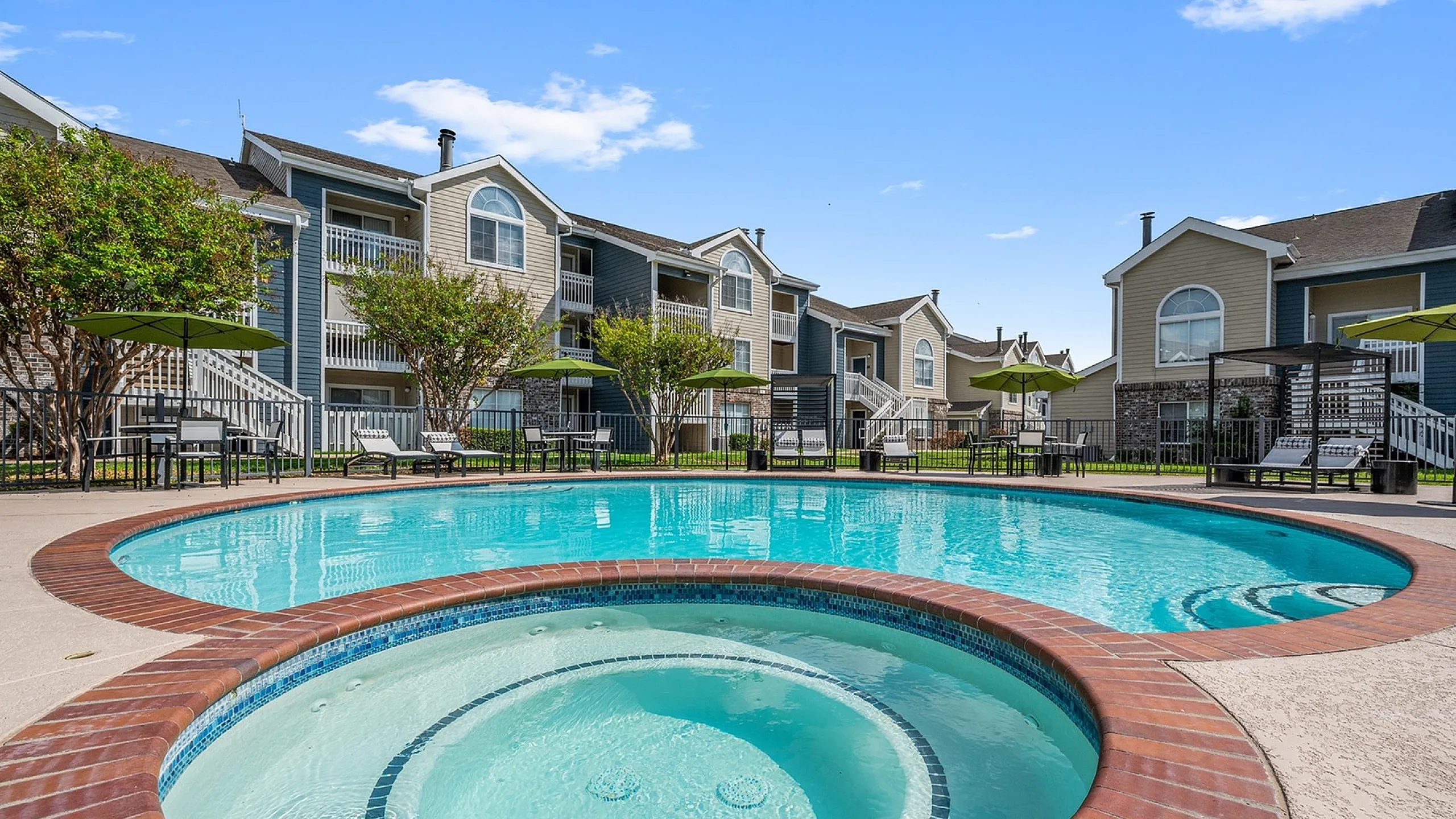 Inviting apartment complex with a sparkling pool and hot tub surrounded by lush greenery, perfect for relaxation and recreation.