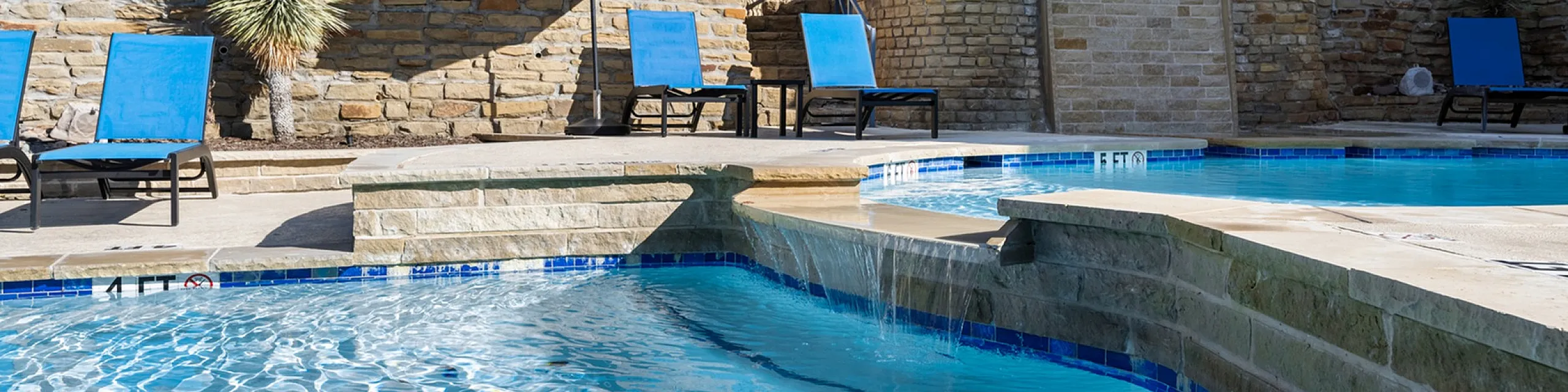 Inviting outdoor swimming pool area with elegant lounge chairs and stone accents under a clear blue sky.