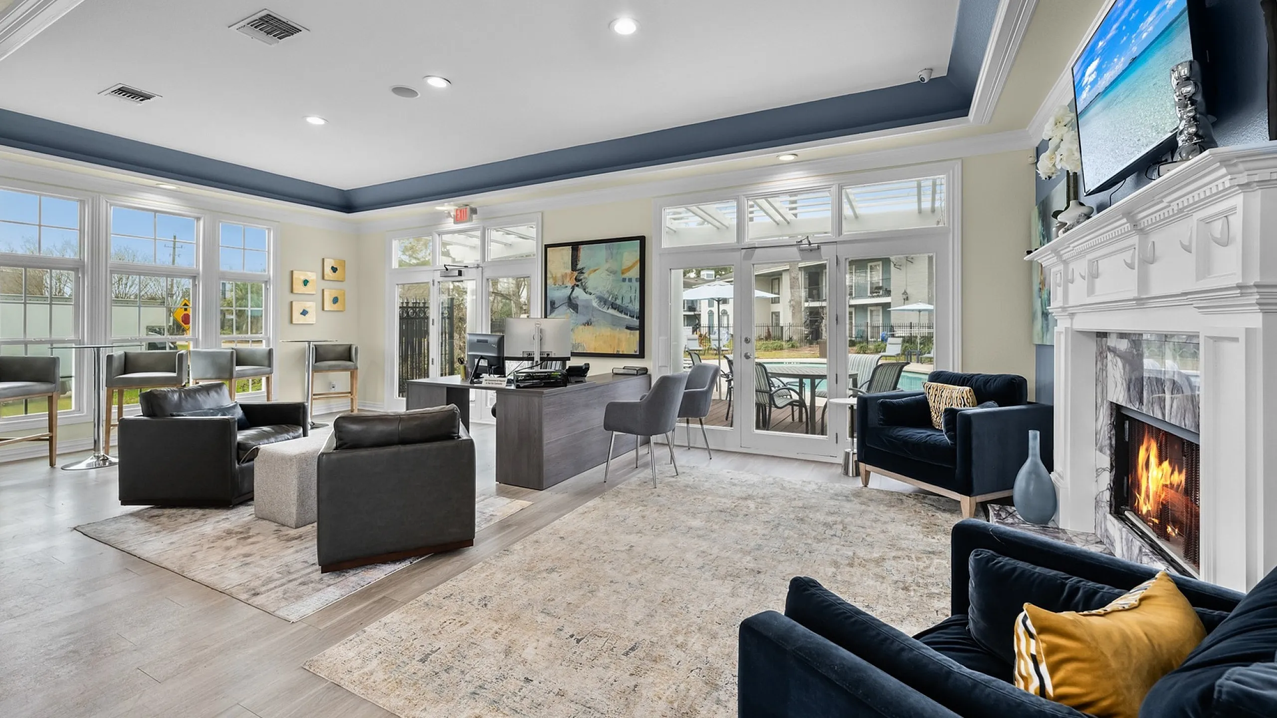 Bright and inviting lounge area with modern decor, cozy seating, a fireplace, and large windows overlooking the pool.