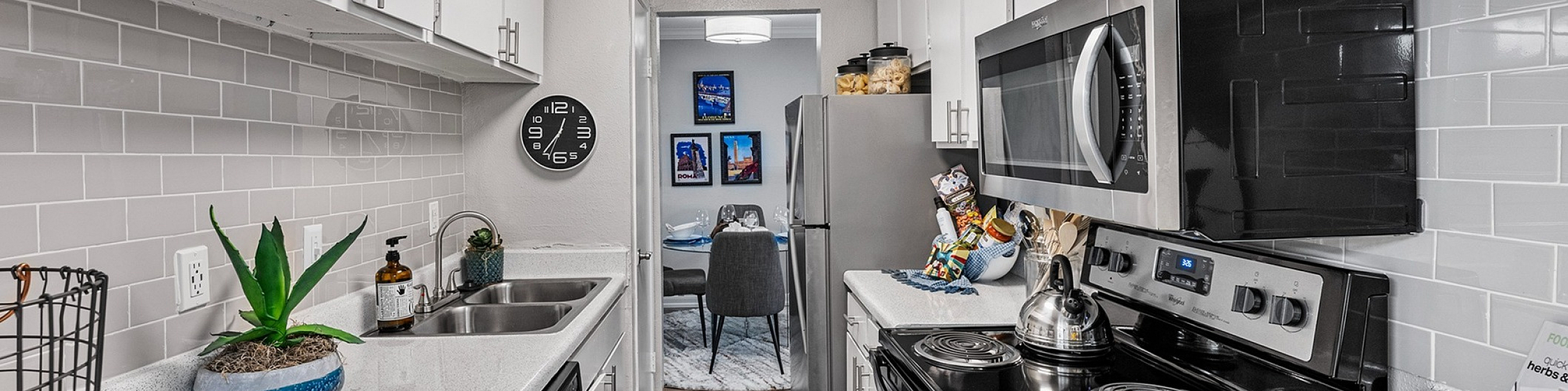Modern galley kitchen featuring sleek white cabinetry, stainless steel appliances, and elegant tiled backsplash with a cozy dining area view.