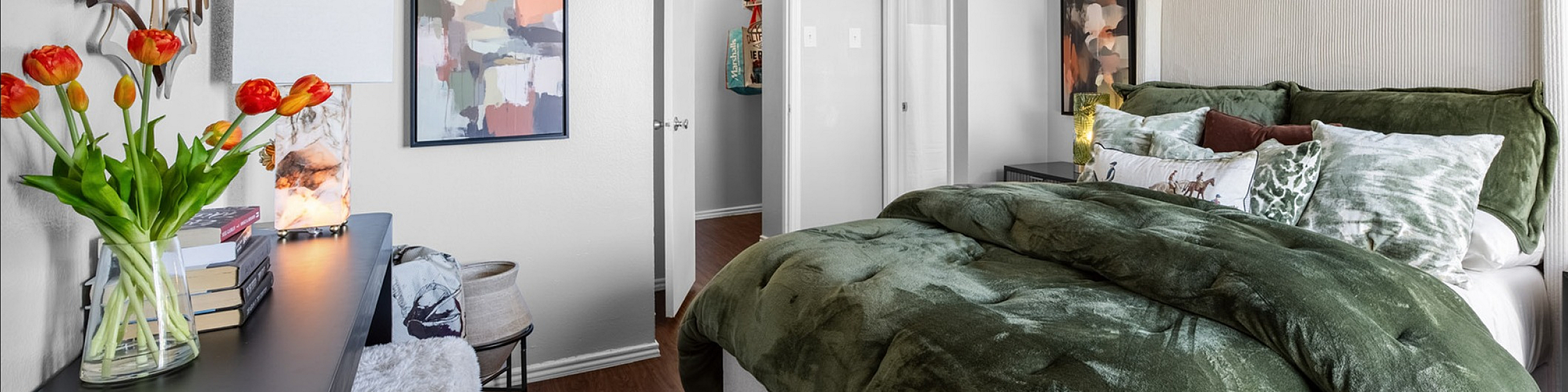 Inviting bedroom featuring a plush green comforter, elegant wall art, and accent lamps, creating a cozy and stylish atmosphere.