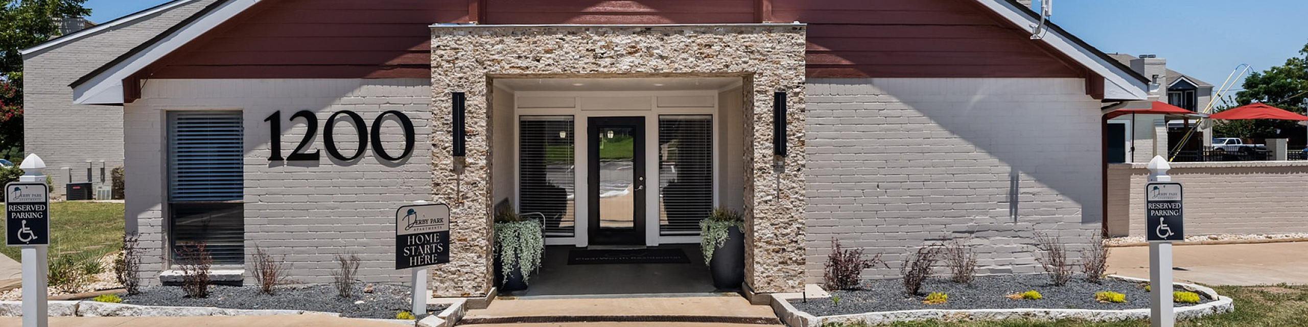 Inviting entrance to modern apartment complex with stone accents, accessible parking, and welcoming greenery.