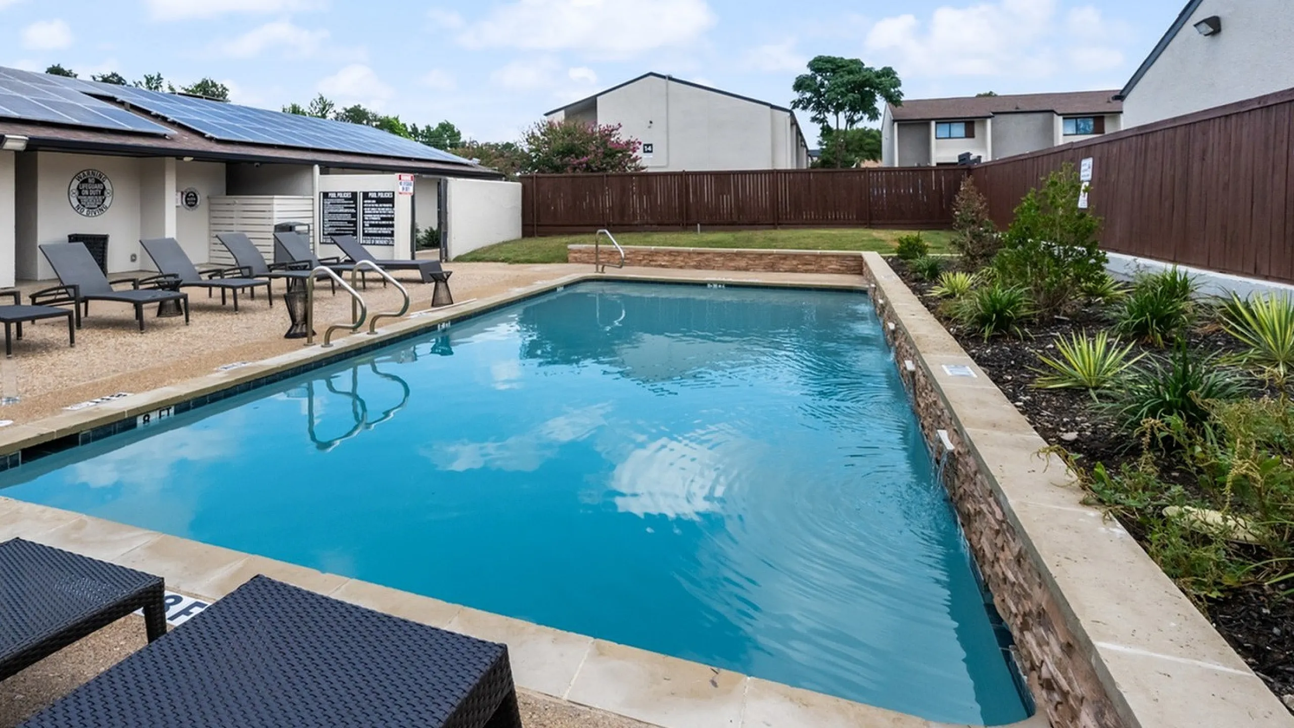 Inviting outdoor swimming pool with sleek loungers, surrounded by lush greenery and contemporary apartment buildings under a bright blue sky.