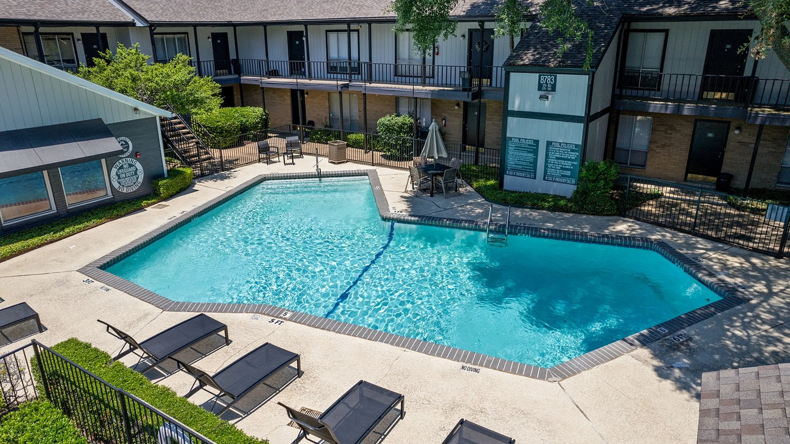 Inviting apartment courtyard featuring a sparkling swimming pool, cozy poolside seating, and lush greenery for relaxation and leisure.