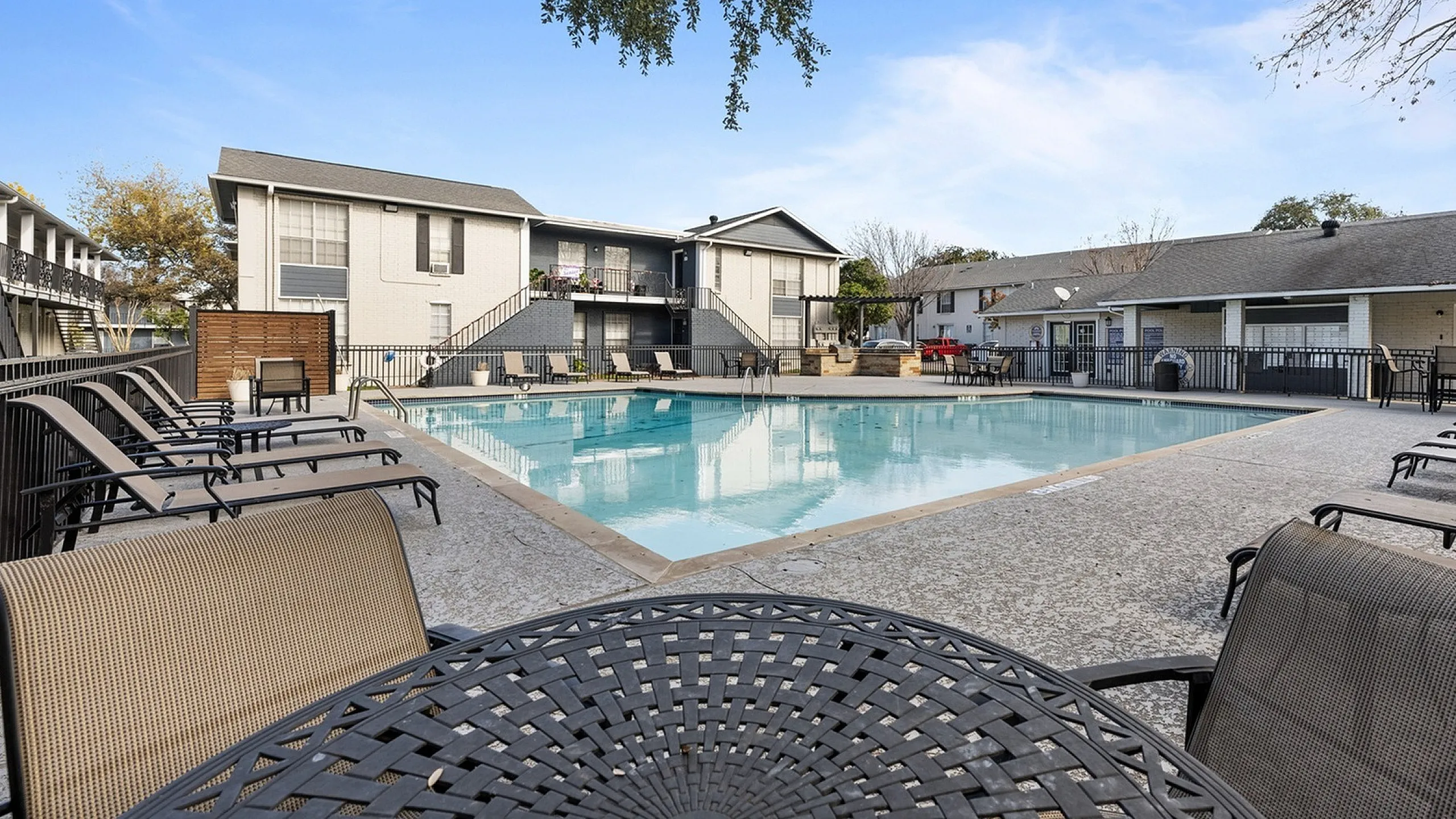 Inviting apartment complex with a pristine outdoor pool surrounded by comfortable lounge chairs and a scenic view, perfect for relaxation.