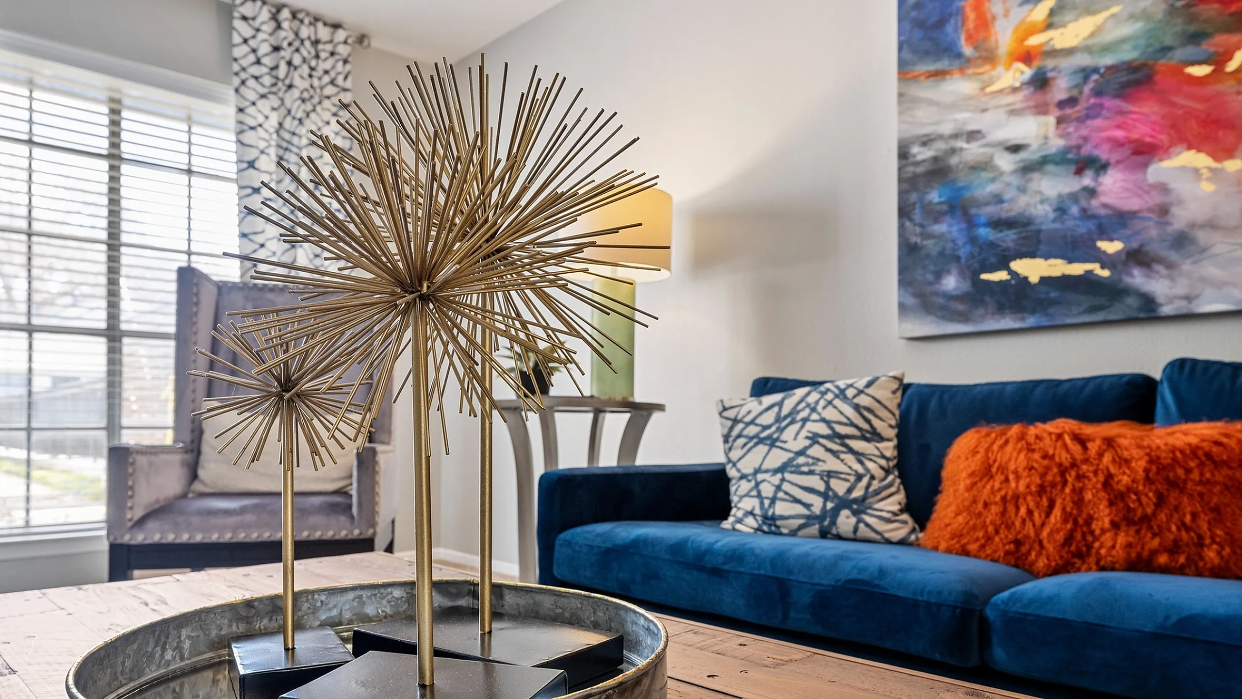 Chic living room with a vibrant blue couch, stylish artwork, and elegant gold decor centerpiece.