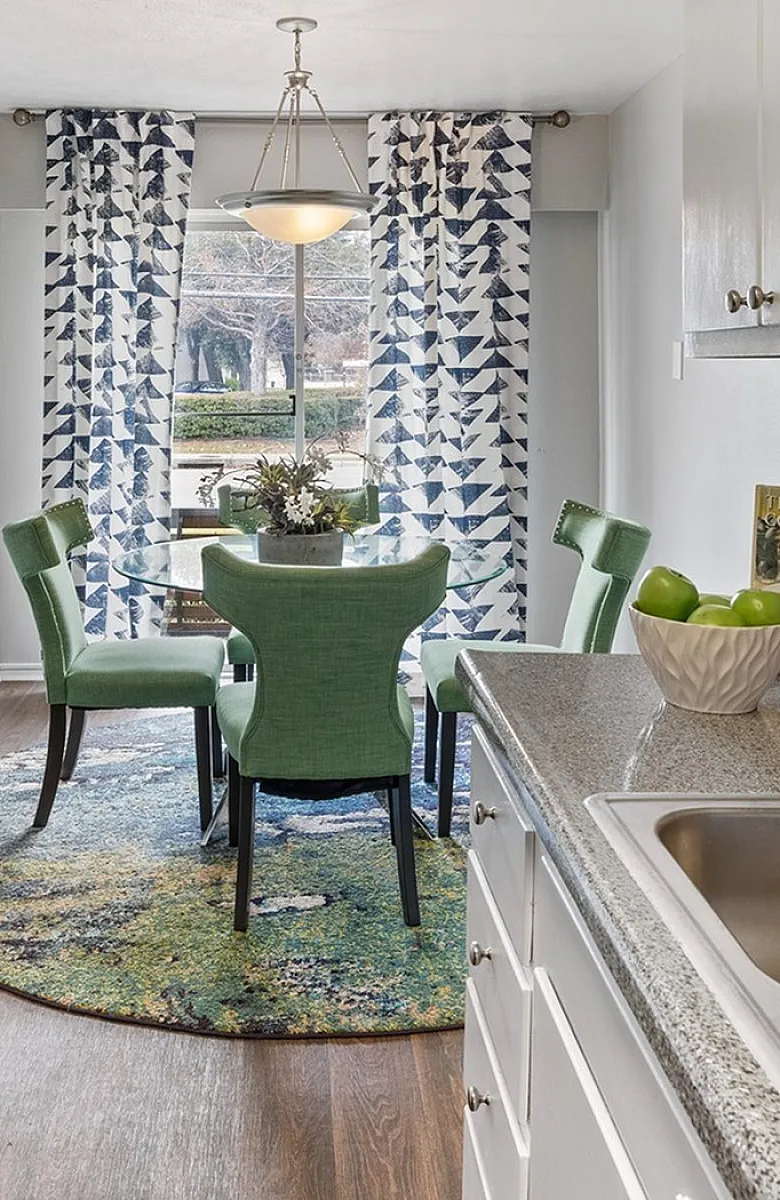 Bright, modern kitchen with sleek appliances, granite countertops, and vibrant green dining set accented by lush plants and artistic decor.