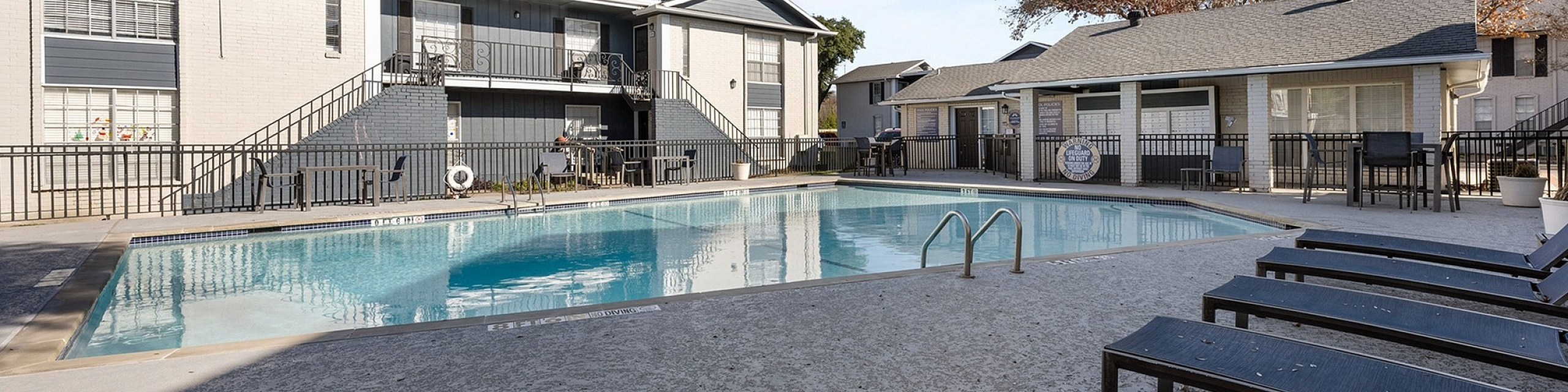 Inviting apartment complex featuring a pristine swimming pool and comfortable lounge chairs under a clear blue sky.