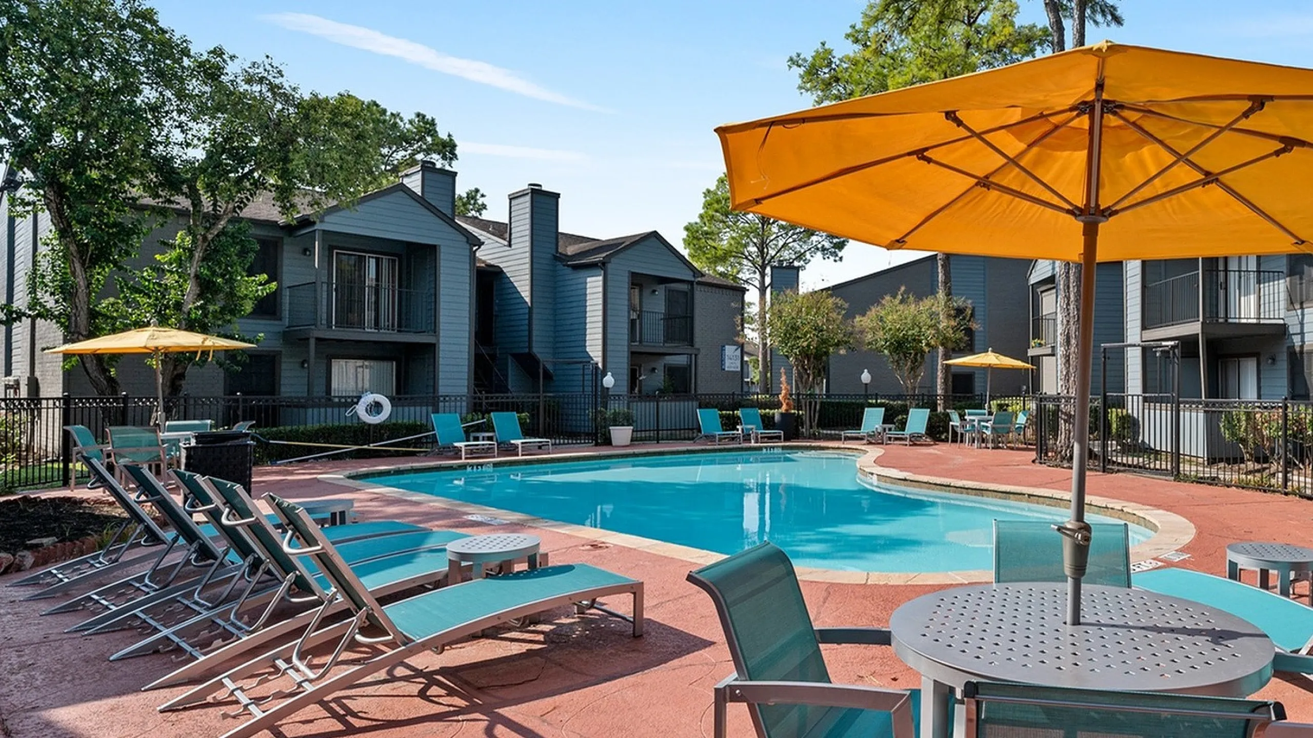 Inviting apartment complex pool area with vibrant yellow umbrellas, modern lounge chairs, and lush surroundings.