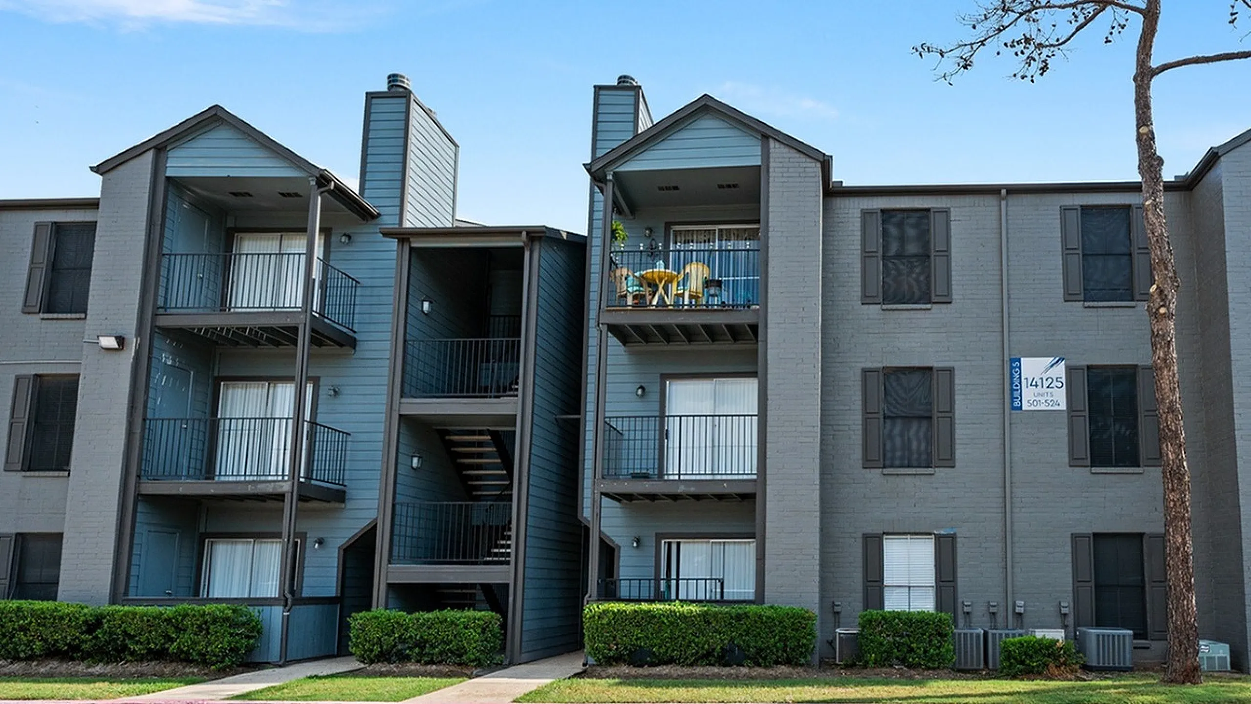 Charming multi-level apartment complex with balconies, lush greenery, and modern exterior in a vibrant neighborhood.