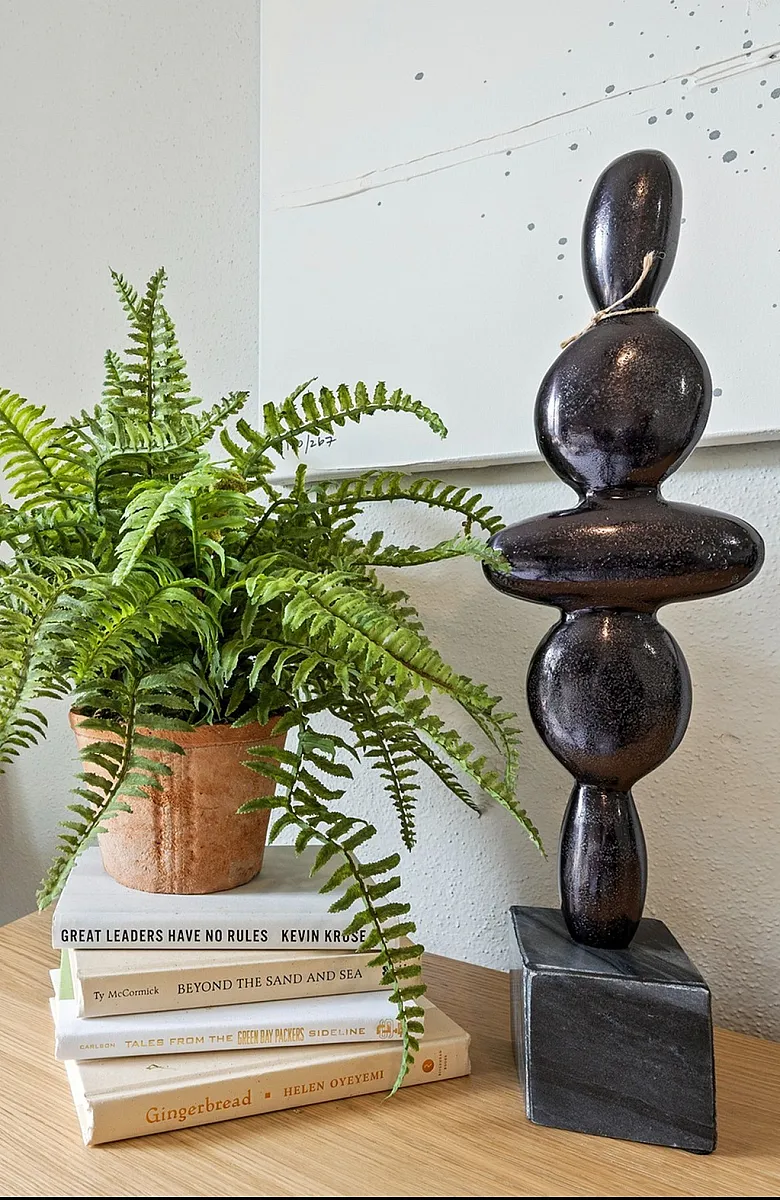 Chic interior decor with a lush green fern, modern sculpture, and cozy pillows on a wooden table, creating a warm and inviting atmosphere.