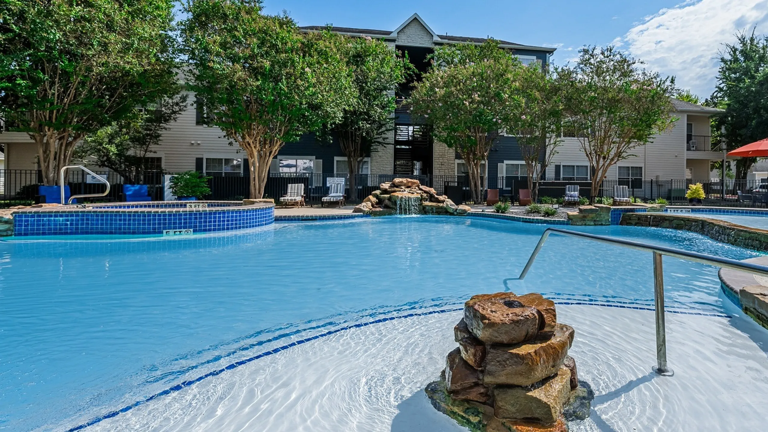 Inviting apartment complex featuring a stunning outdoor pool with a waterfall, surrounded by lush greenery and modern amenities.