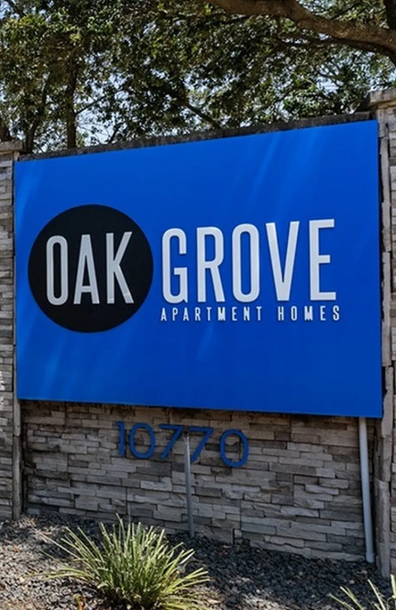 Welcoming Oak Grove Apartment Homes entrance showcasing a stylish sign amidst lush greenery and a modern building backdrop.