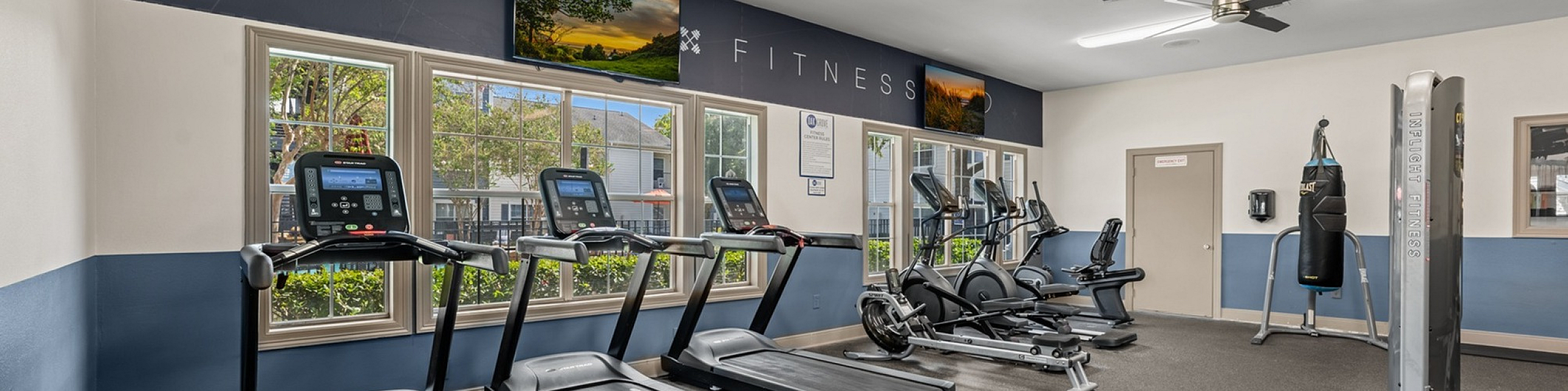 Modern fitness center equipped with treadmills, ellipticals, and boxing bag, featuring natural lighting and sleek design.