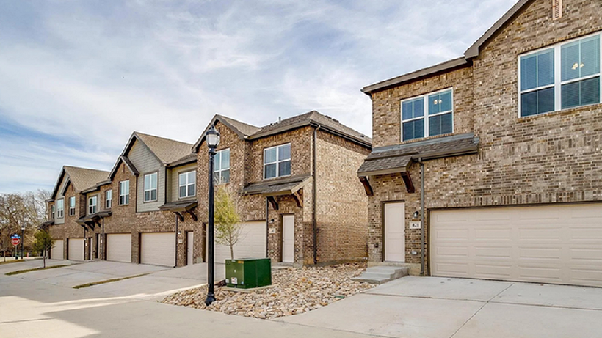 Charming row of modern townhouses with brick facades, spacious driveways, and a serene suburban setting.