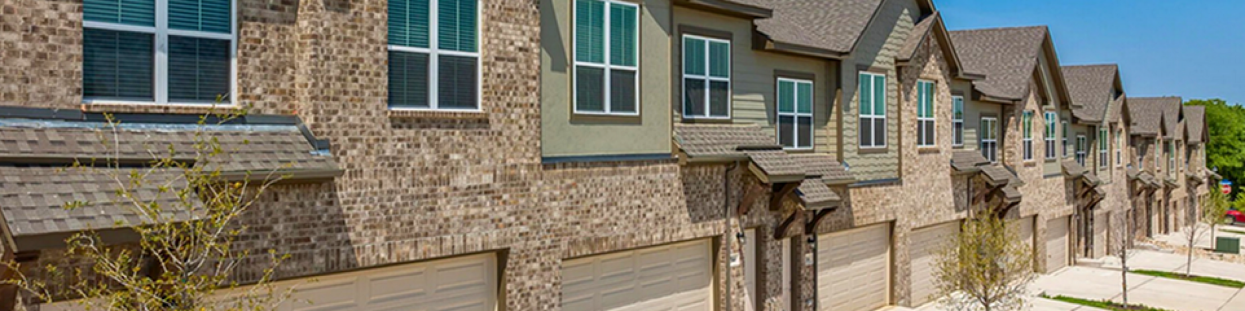 Charming row of modern townhouses with brick facades, featuring double garages and large windows under a clear blue sky.