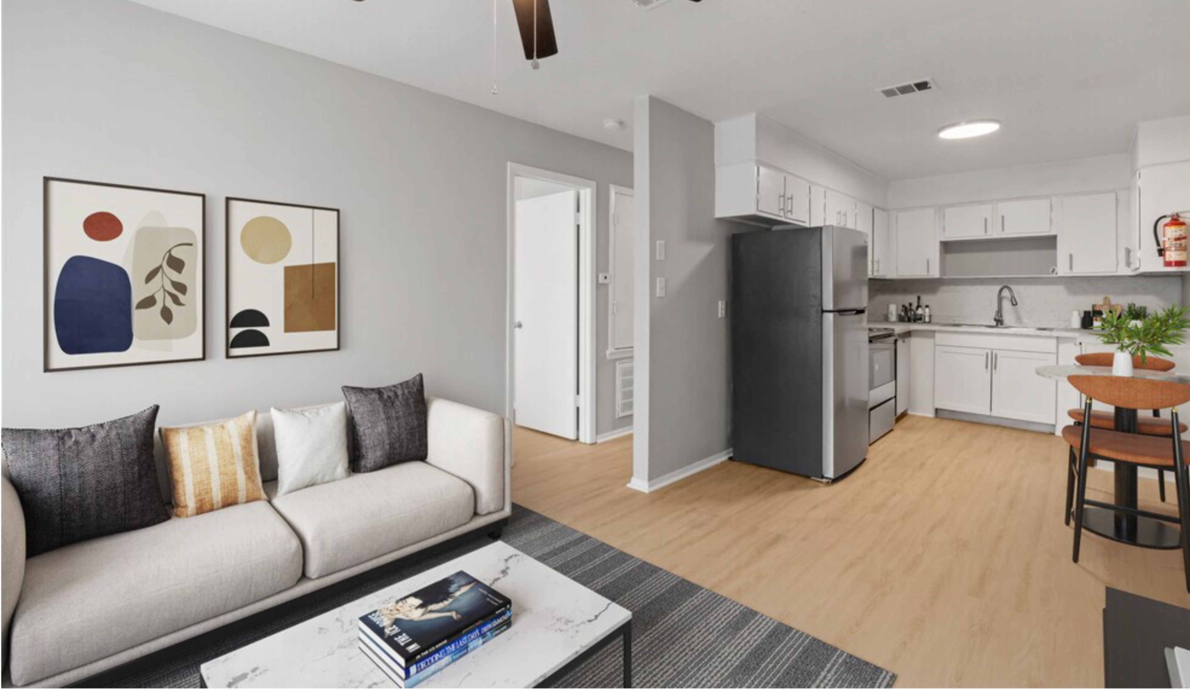 Modern apartment interior with cozy living area, featuring stylish furniture and artwork, adjacent to a sleek, fully-equipped kitchen and dining space.