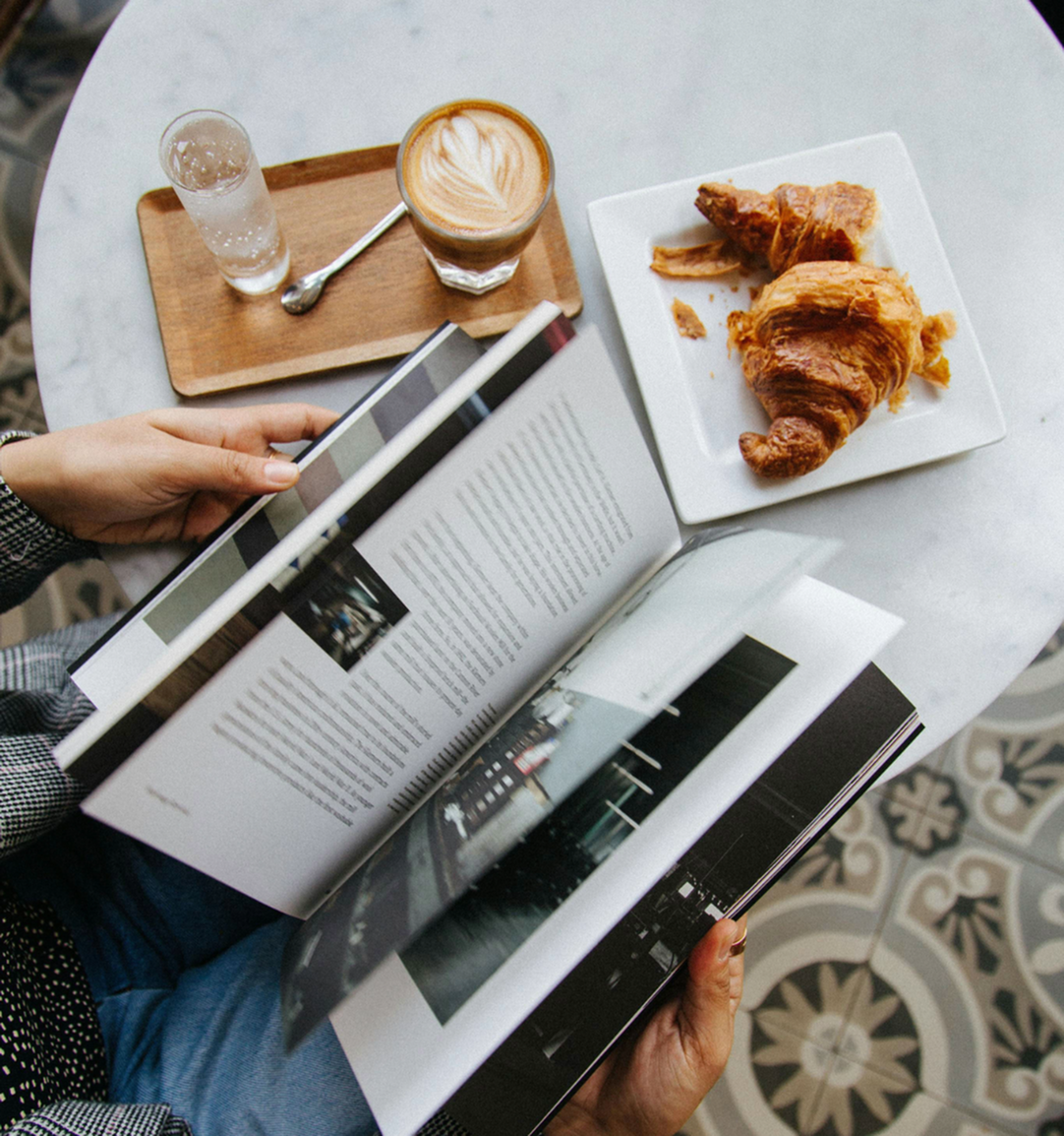 Cozy coffee moment with an open book next to a latte and croissant on a stylish tiled table.