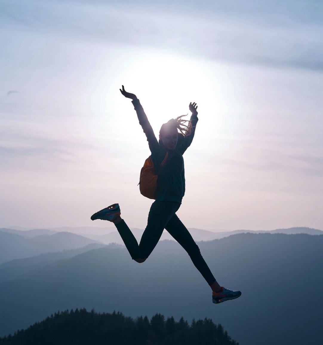 Energized hiker leaps joyfully against a stunning mountain sunrise backdrop.