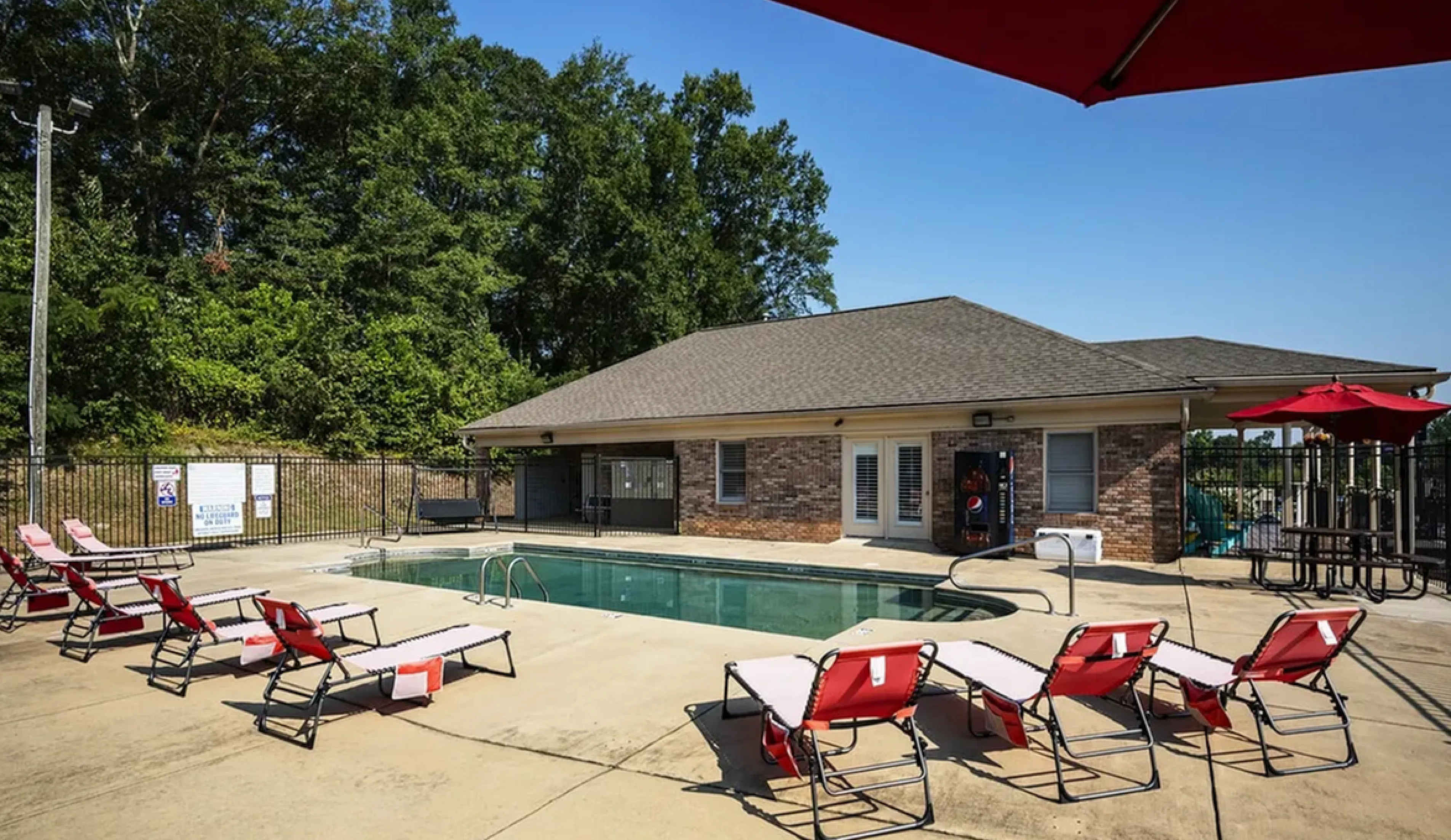 Inviting outdoor pool area with red sun loungers and umbrellas, surrounded by lush greenery, offering a relaxing retreat.