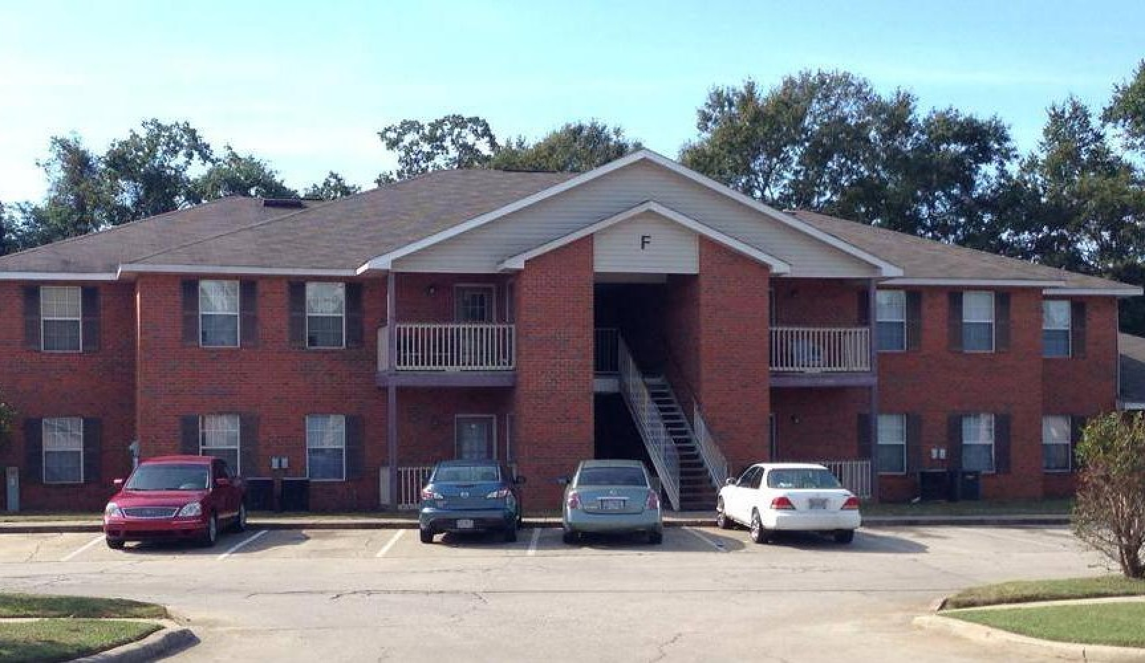 Elegant brick apartment building with convenient parking, surrounded by lush greenery and featuring charming balconies.
