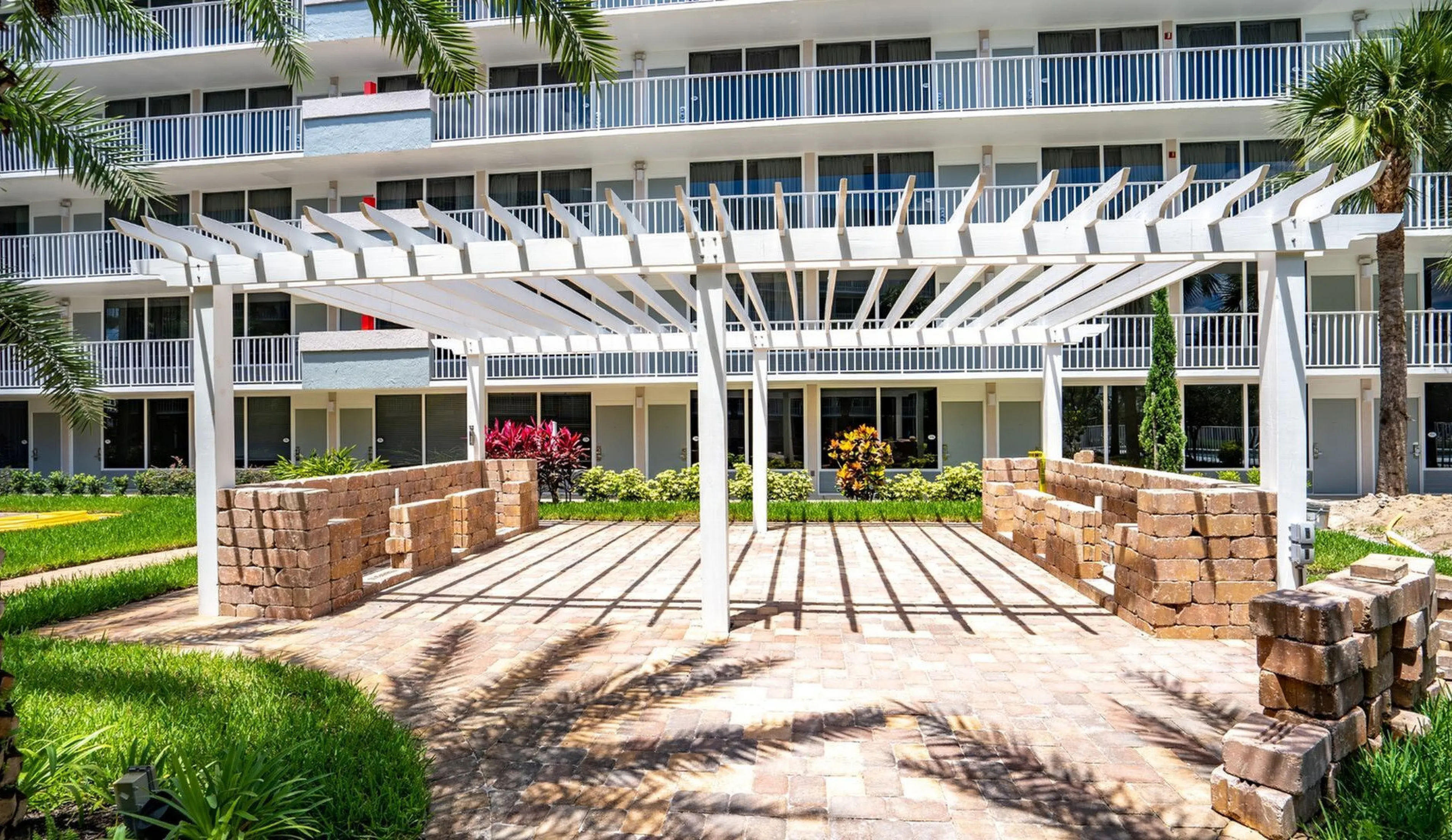 Charming outdoor space with a white pergola and lush landscaping in front of a modern apartment building with balconies.