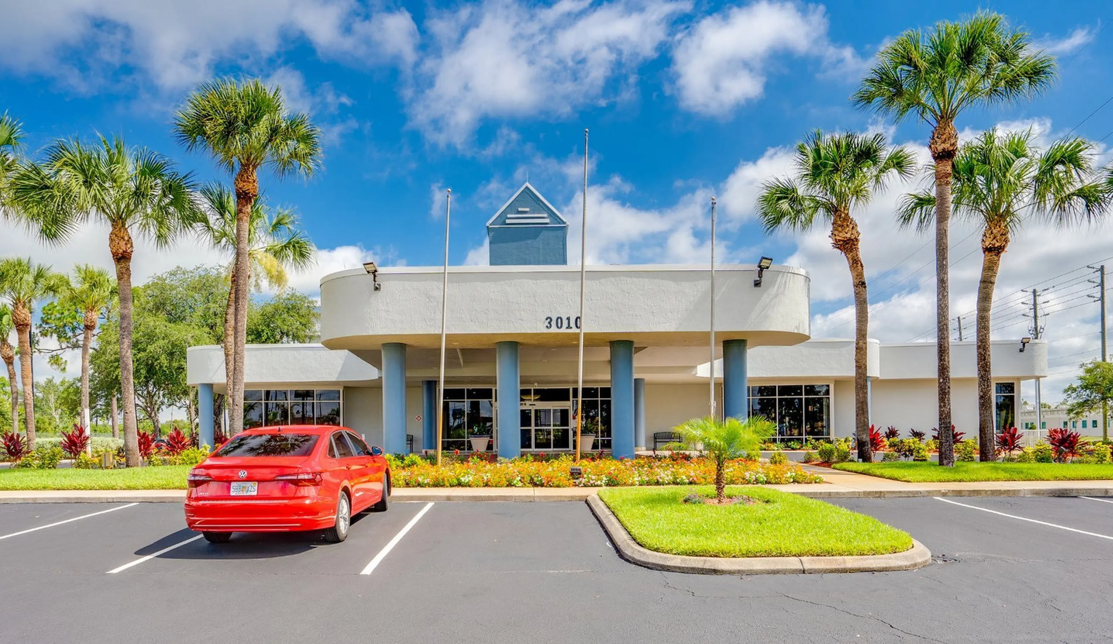 Inviting apartment complex entrance with modern architecture, lush palm trees, and vibrant landscaping under a clear blue sky.