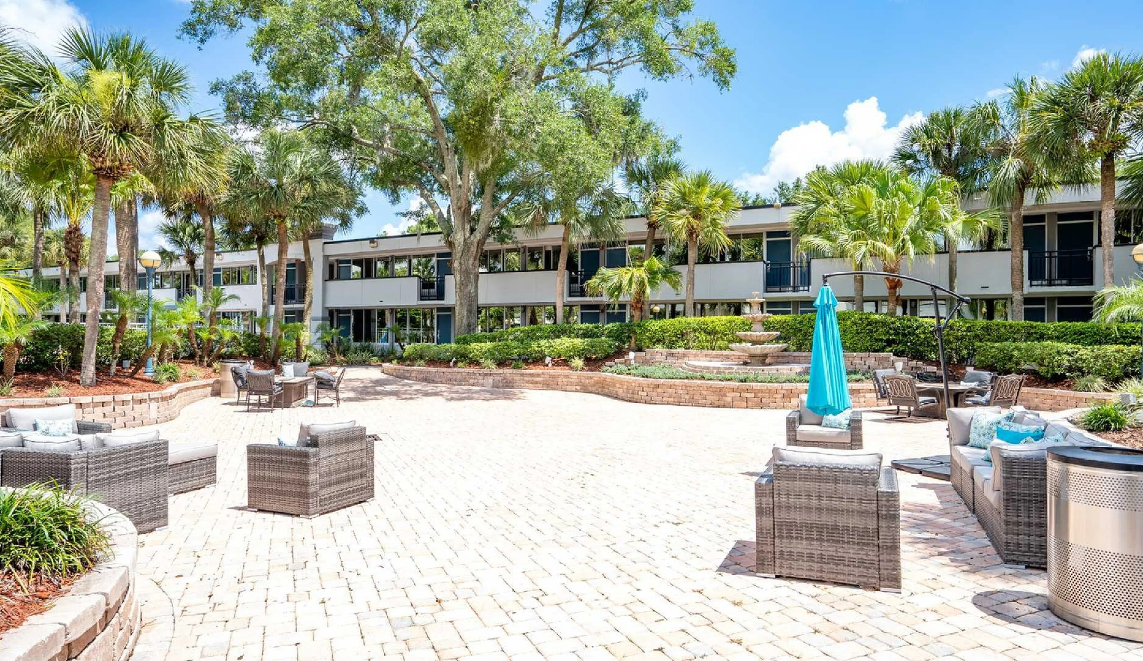 Luxurious outdoor courtyard with modern seating, surrounded by lush palm trees and a charming two-story apartment complex.