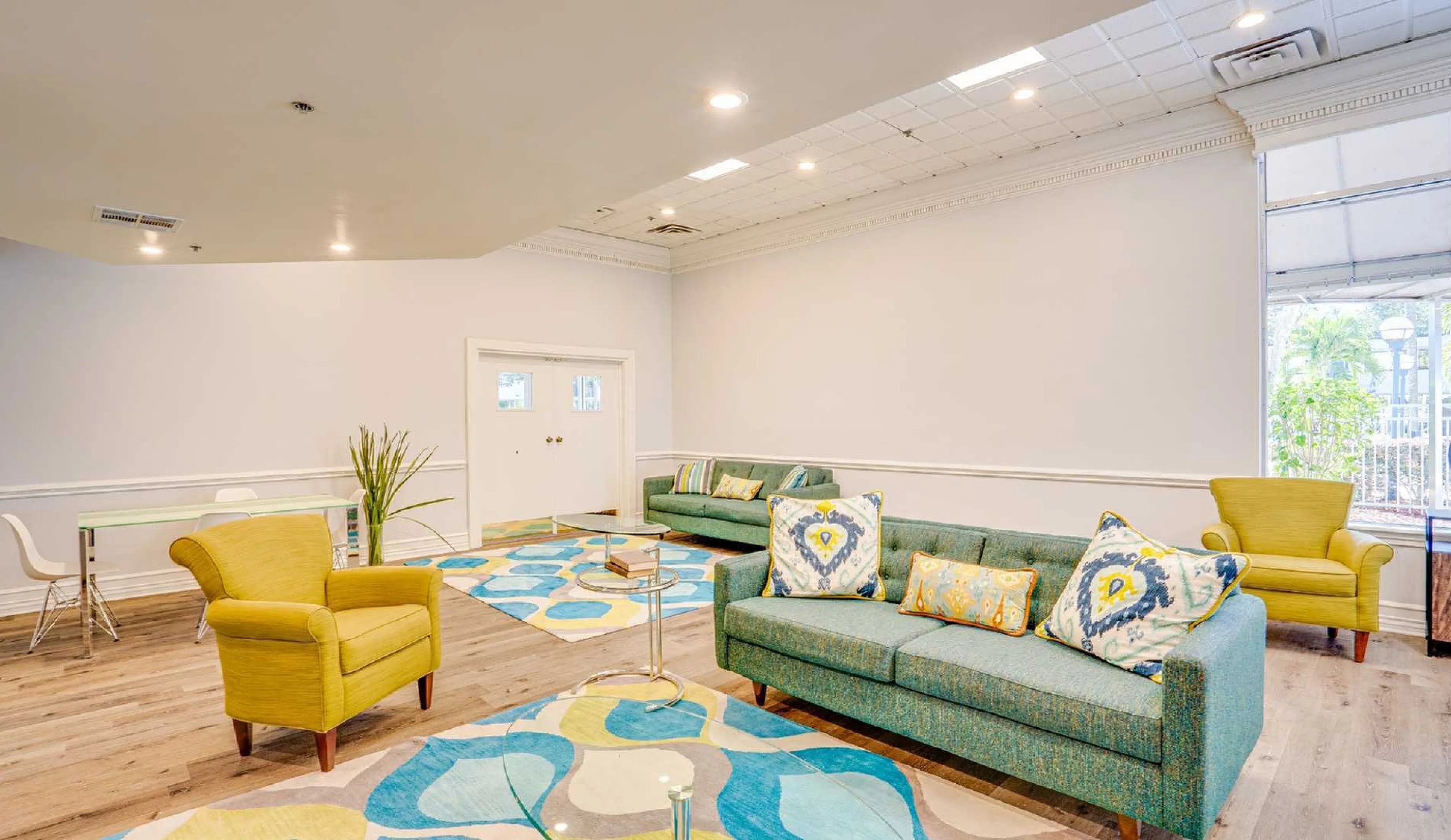Inviting living room with stylish decor, featuring vibrant yellow armchairs, elegant blue sofas, and a chic glass coffee table, illuminated by soft recessed lighting.