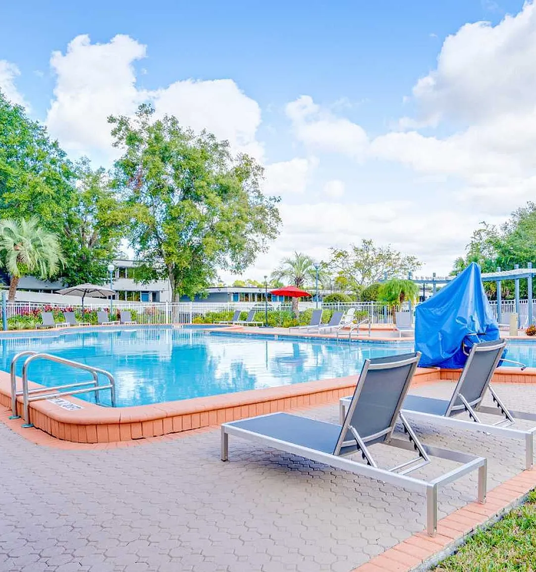 Inviting outdoor pool area with lush greenery, sun loungers, and a serene atmosphere under a bright blue sky.