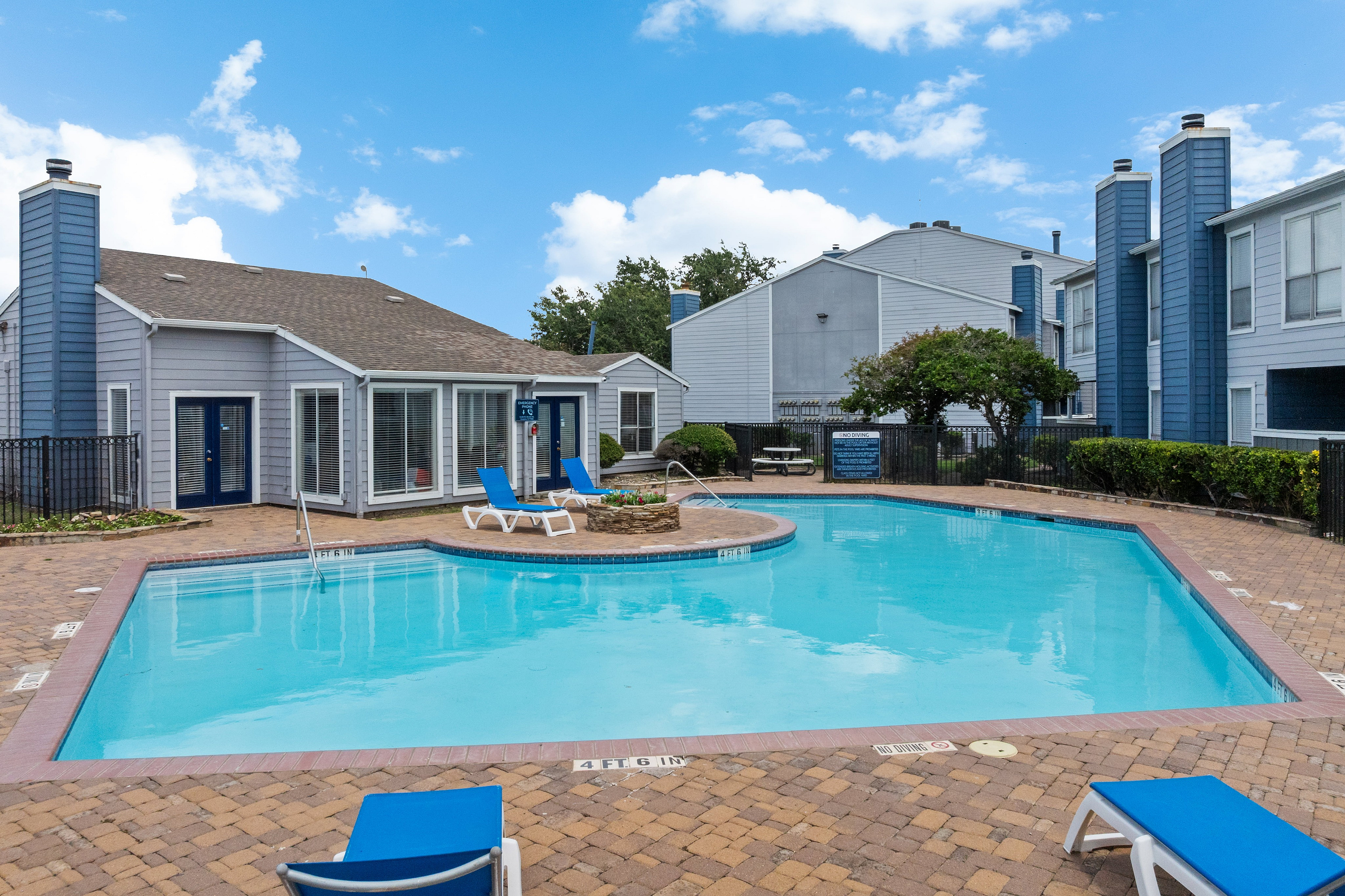 Charming apartment complex featuring a tranquil swimming pool, sun loungers, and cozy blue exterior, perfect for relaxation and leisure.