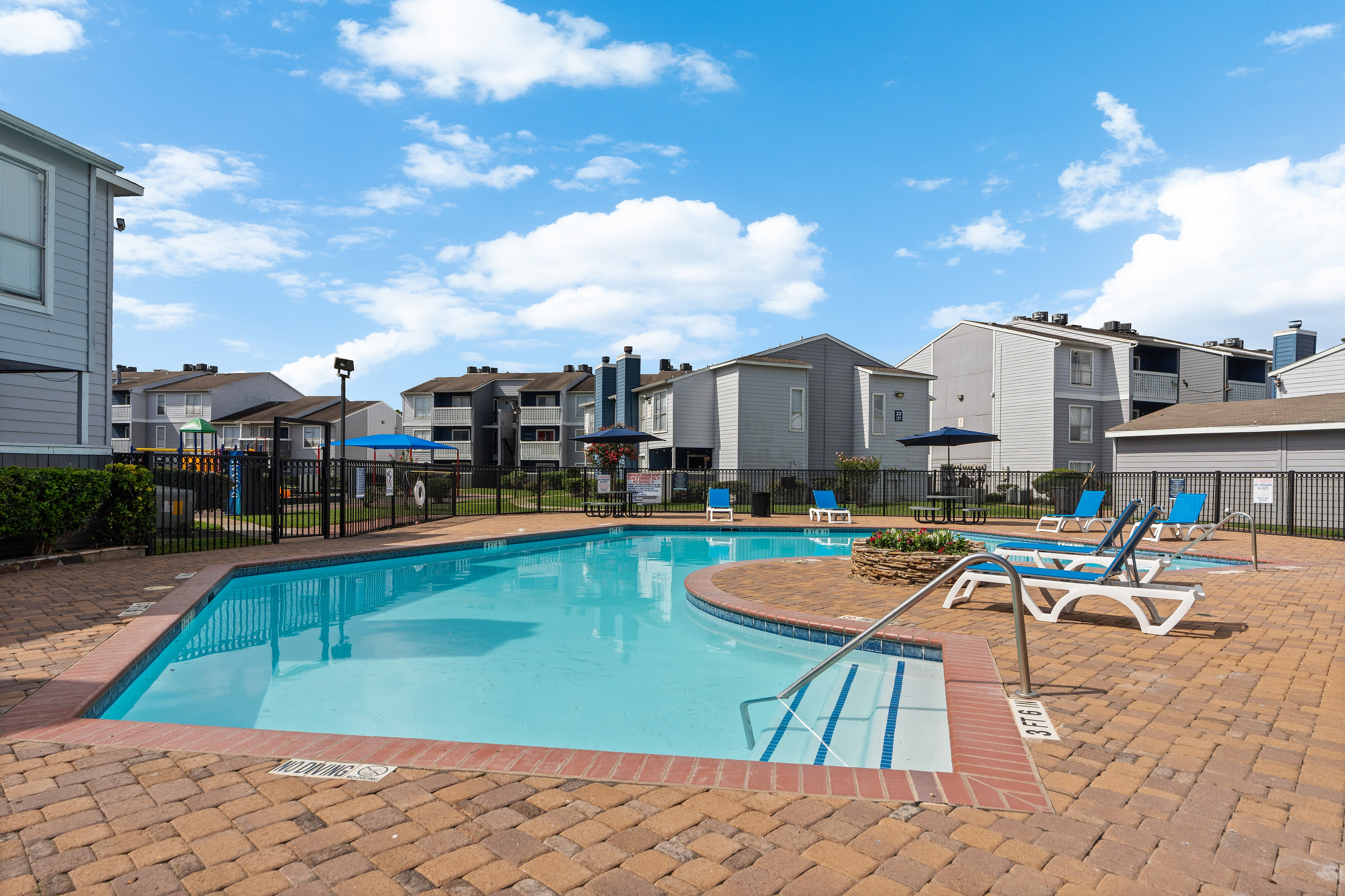 Inviting apartment complex pool area with bright lounge chairs and a clear blue sky, perfect for relaxation.