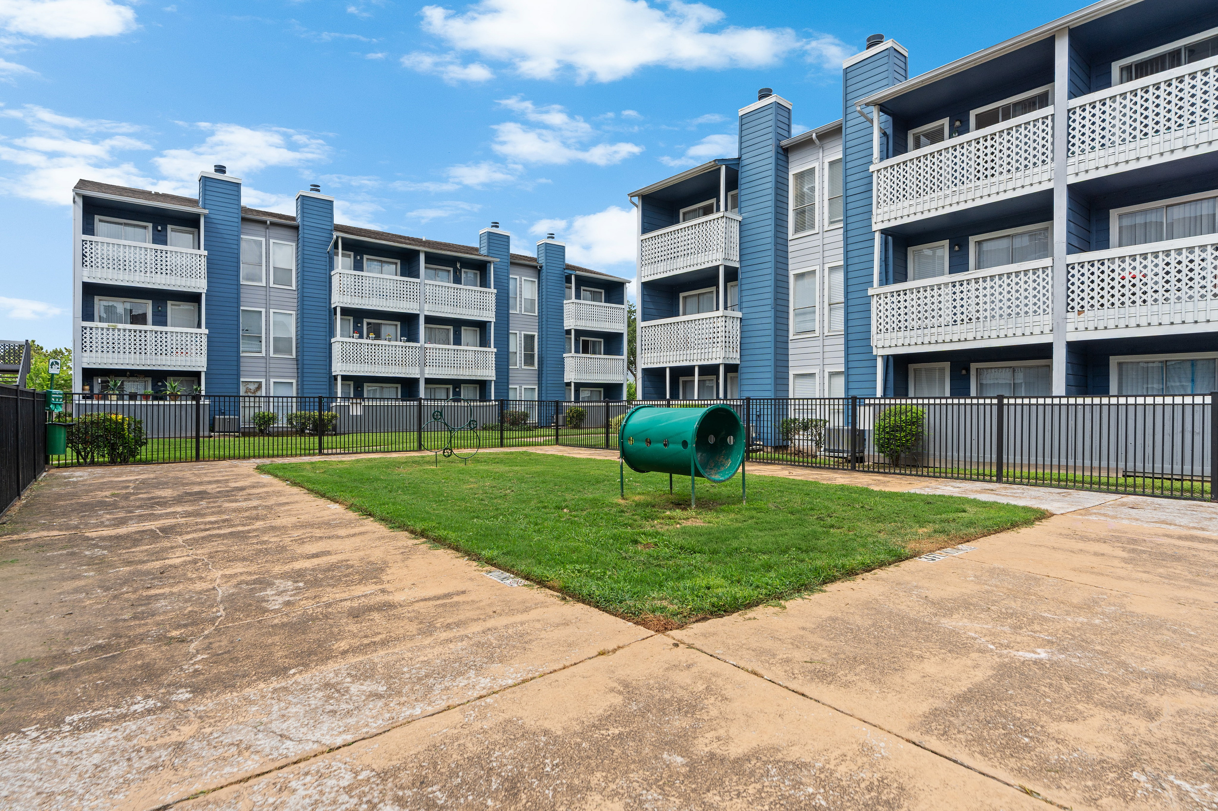 Inviting apartment complex with charming blue and white exterior, featuring private balconies and a fenced grassy area perfect for outdoor enjoyment.