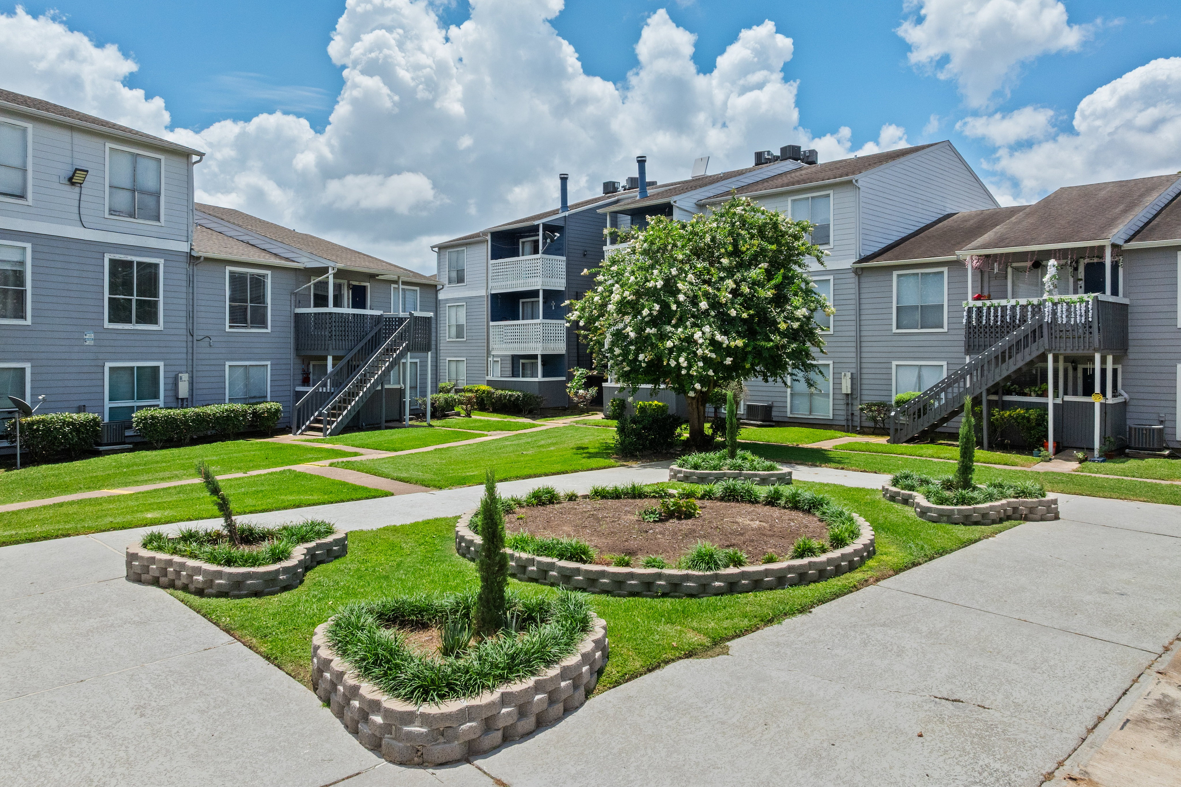Charming apartment complex with landscaped gardens and vibrant greenery under a picturesque sky.