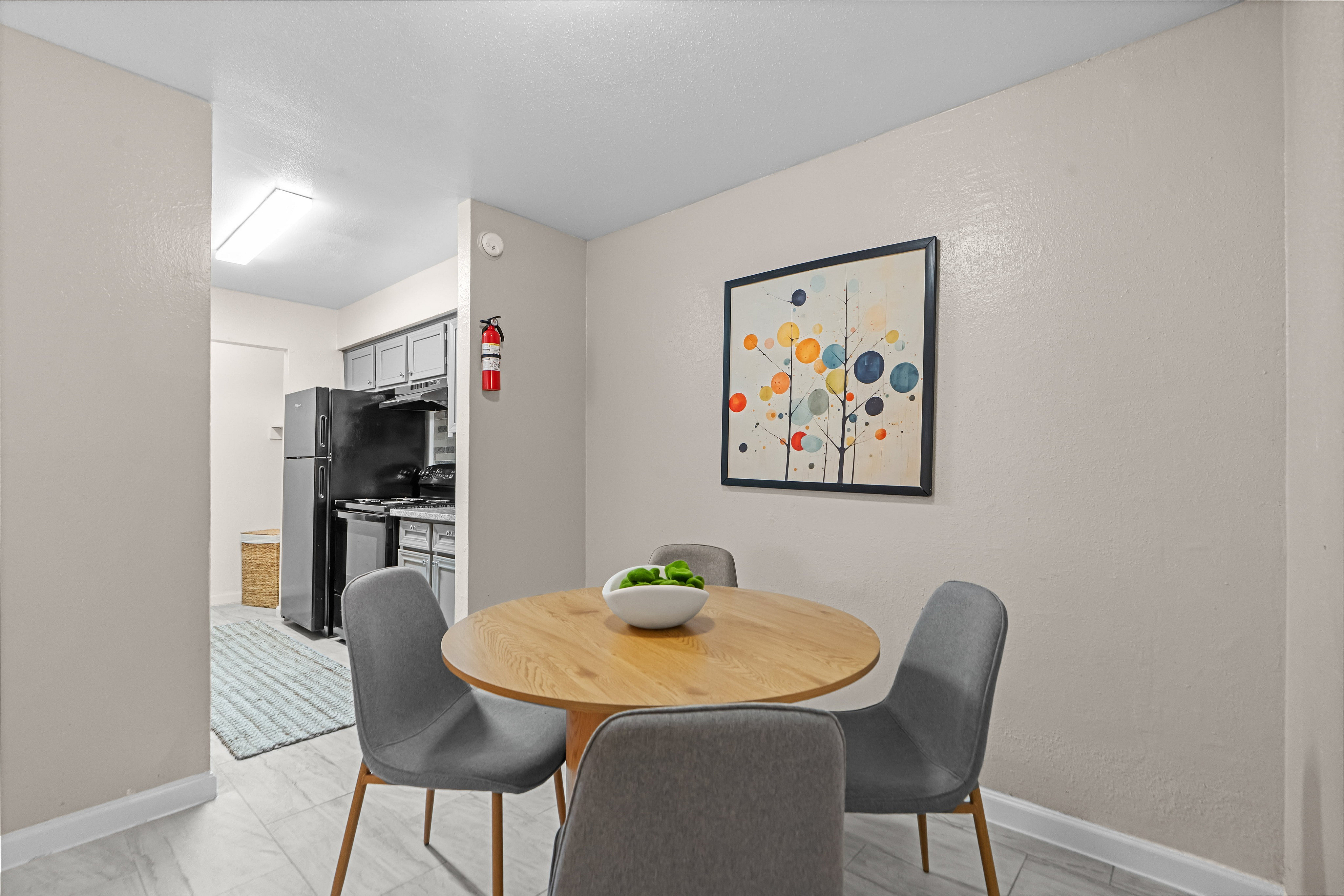 Inviting dining area with a modern wooden table, sleek gray chairs, vibrant wall art, and a view into a contemporary kitchen.