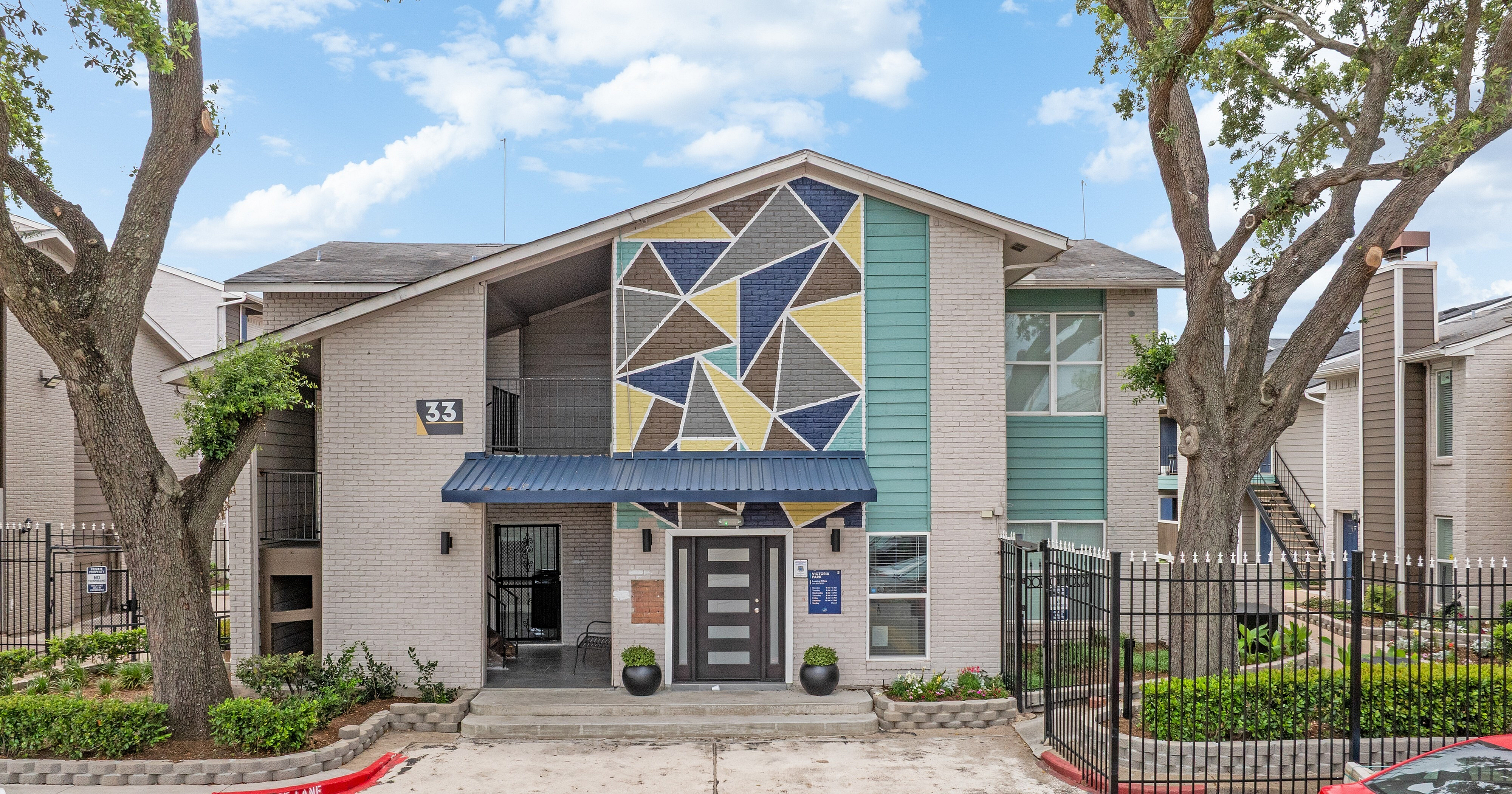 Modern apartment exterior with artistic geometric mural, nestled among lush greenery and elegant fencing.