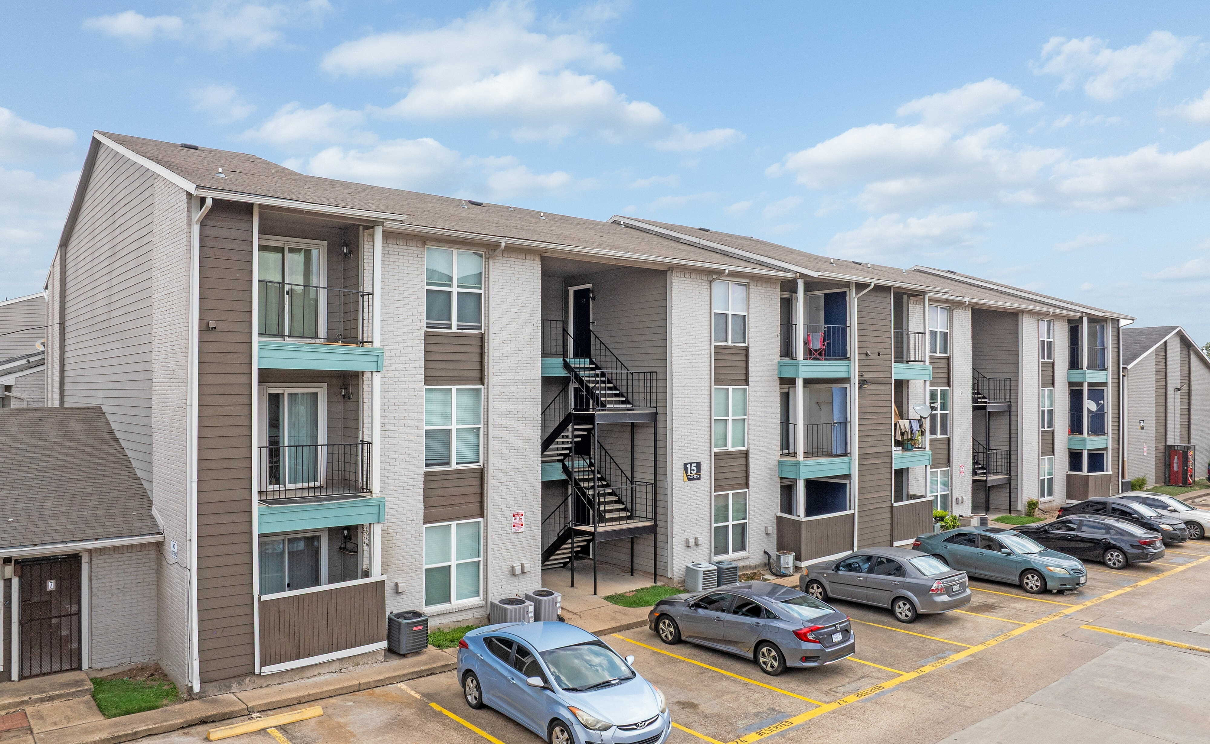 Contemporary three-story apartment building with spacious balconies, modern facade, and ample parking under a clear blue sky.