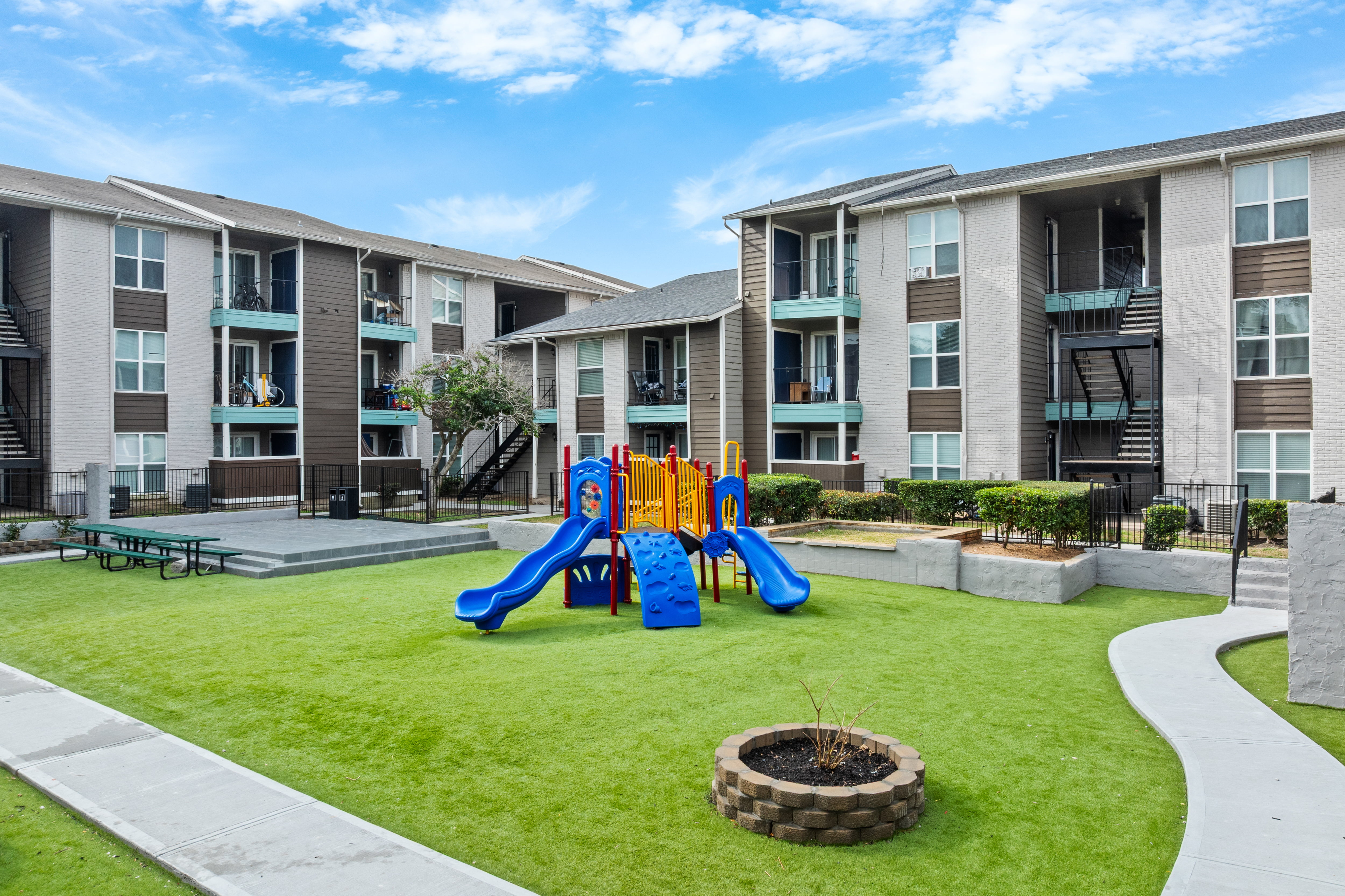 Modern apartment complex with a vibrant children's play area, featuring blue slides and lush green lawns, ideal for family living.