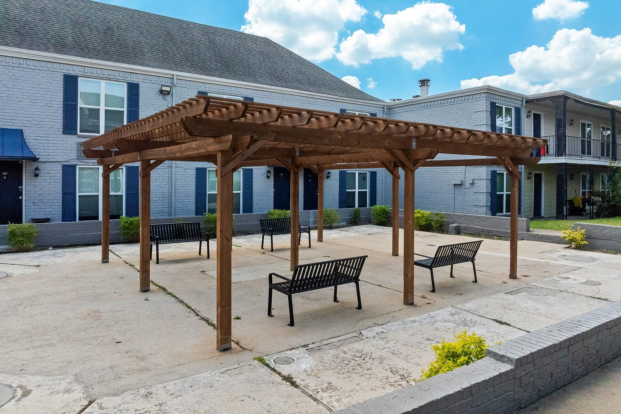 Charming outdoor patio with wooden pergola and modern seating, offering a relaxing communal space in a well-kept apartment complex.