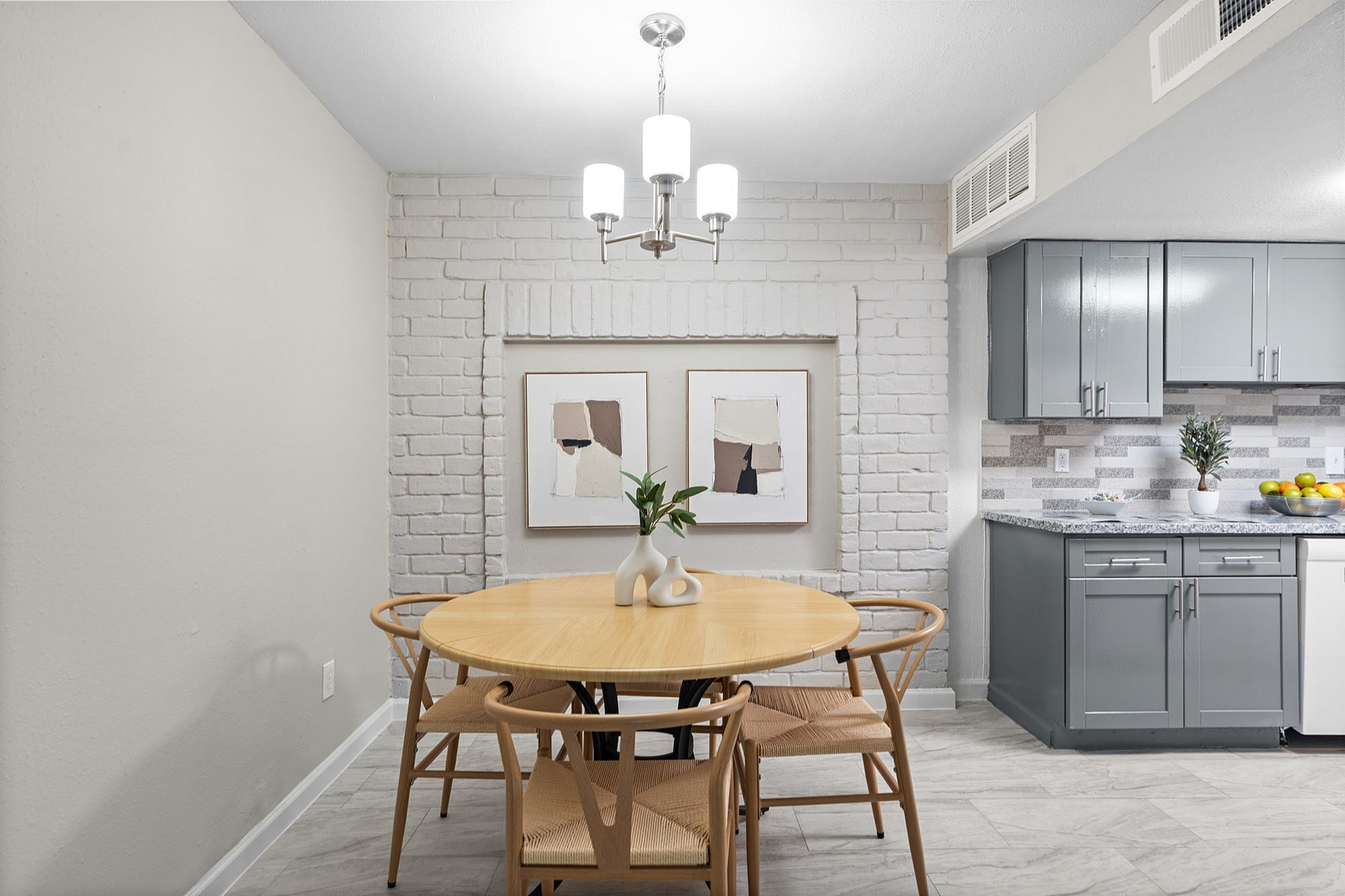 Charming dining area with round wooden table, modern grey kitchen cabinets, and stylish art on a white brick wall.